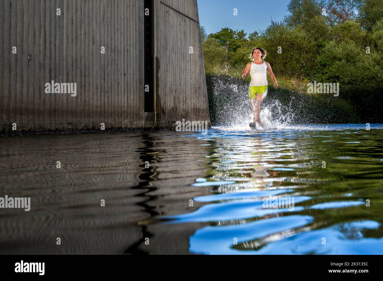 Young woman running through river water in front of tree Stock Photo