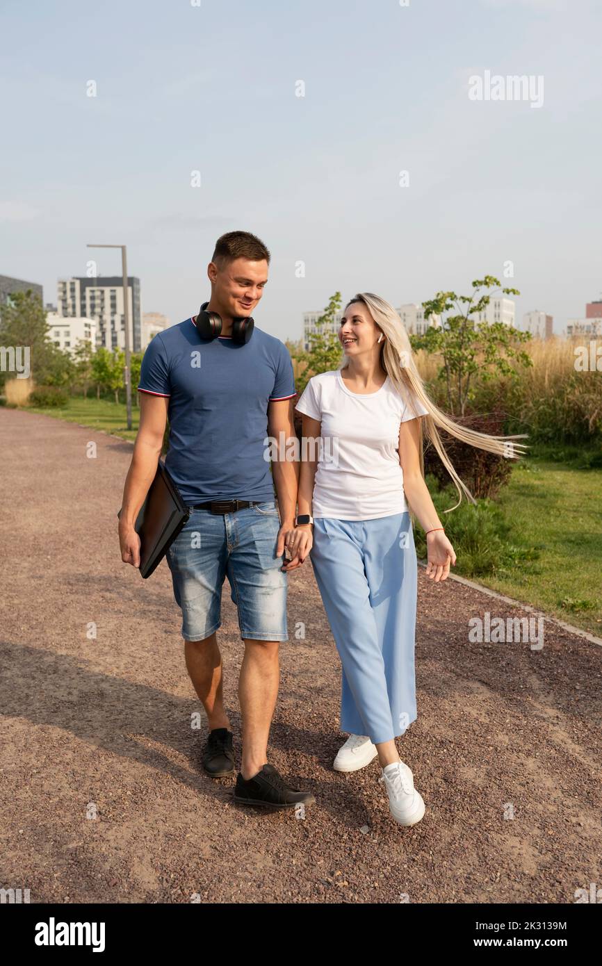 Happy boyfriend and girlfriend walking together holding hands in park Stock Photo