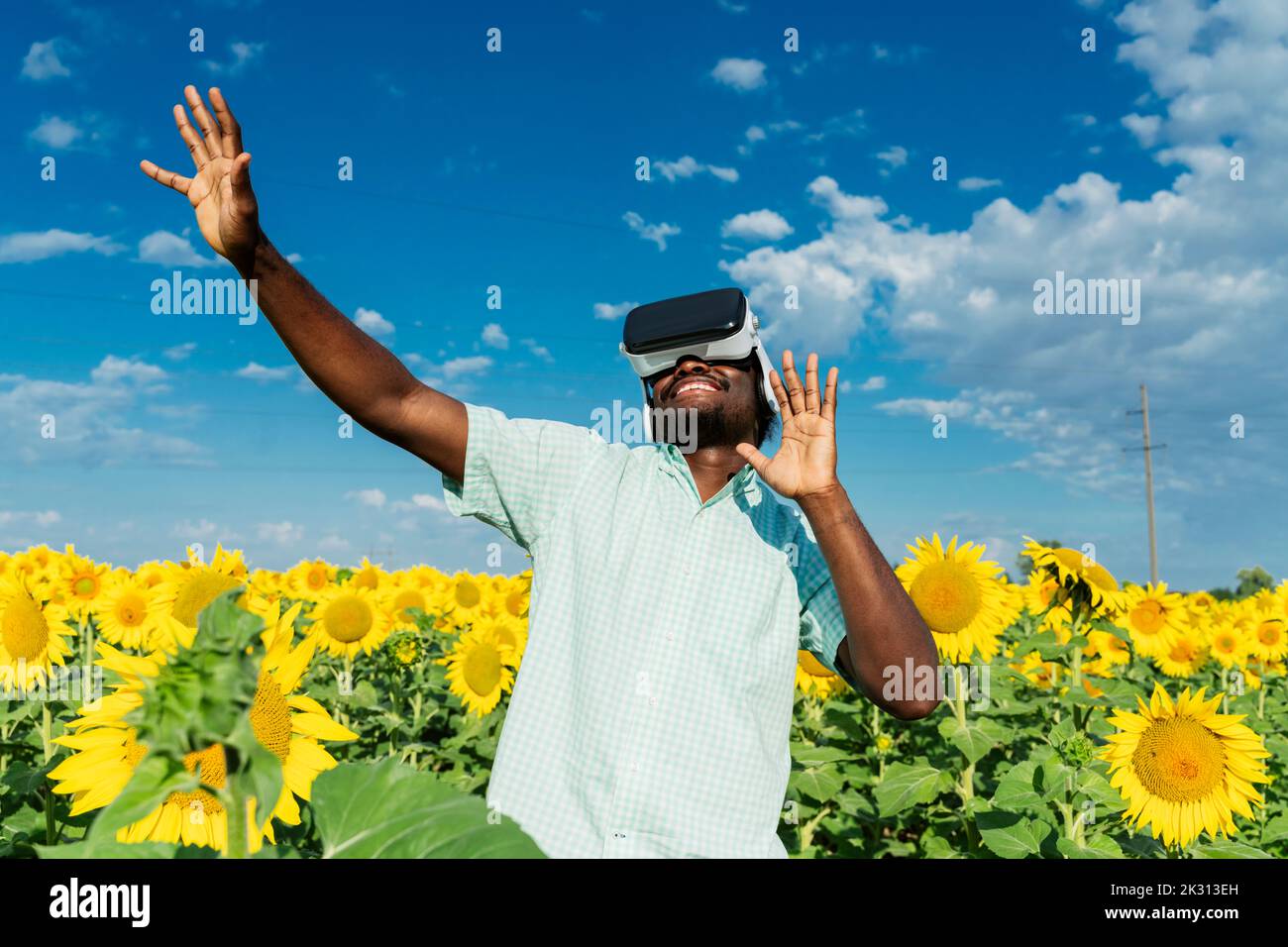Smiling young man wearing virtual reality simulator dancing in sunflower field Stock Photo