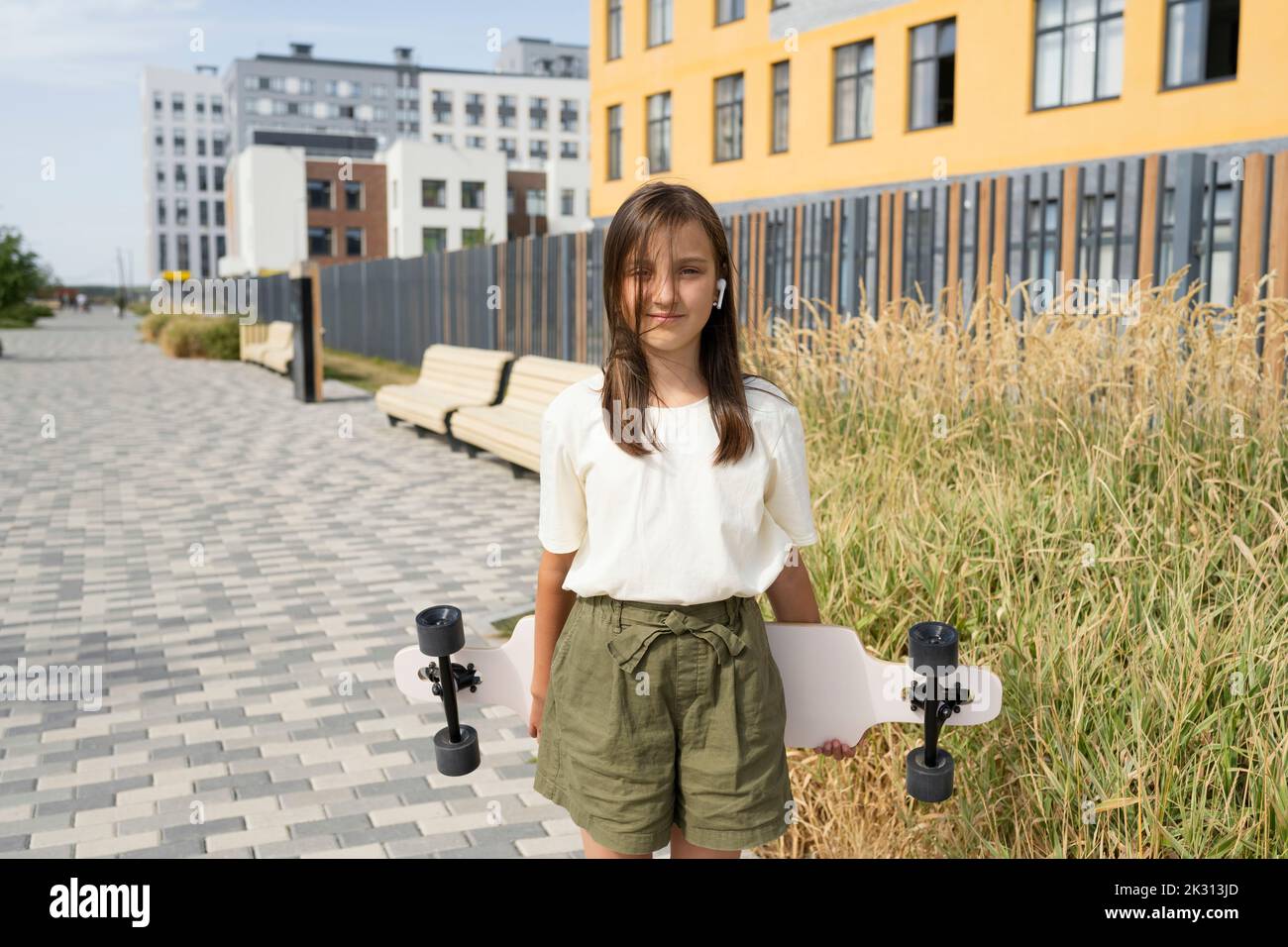 Smiling girl standing with skateboard on footpath Stock Photo