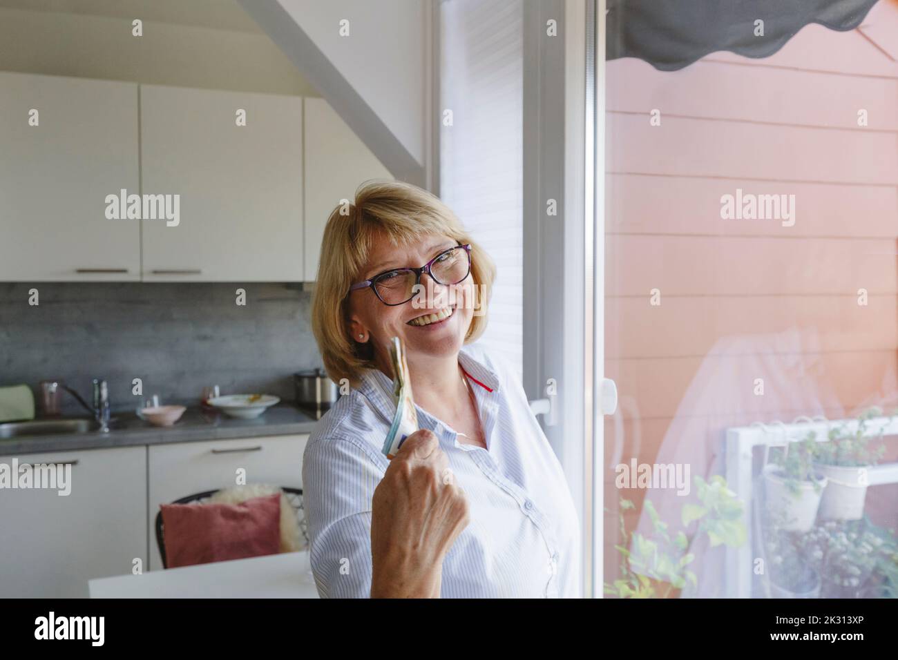 Happy senior woman with paper currency standing at home Stock Photo