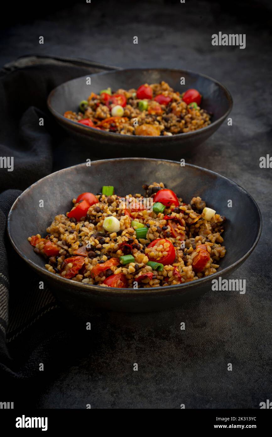 Studio shot of two bowls of bulgur with beluga lentils, tomatoes, peppers, eggplant and scallion