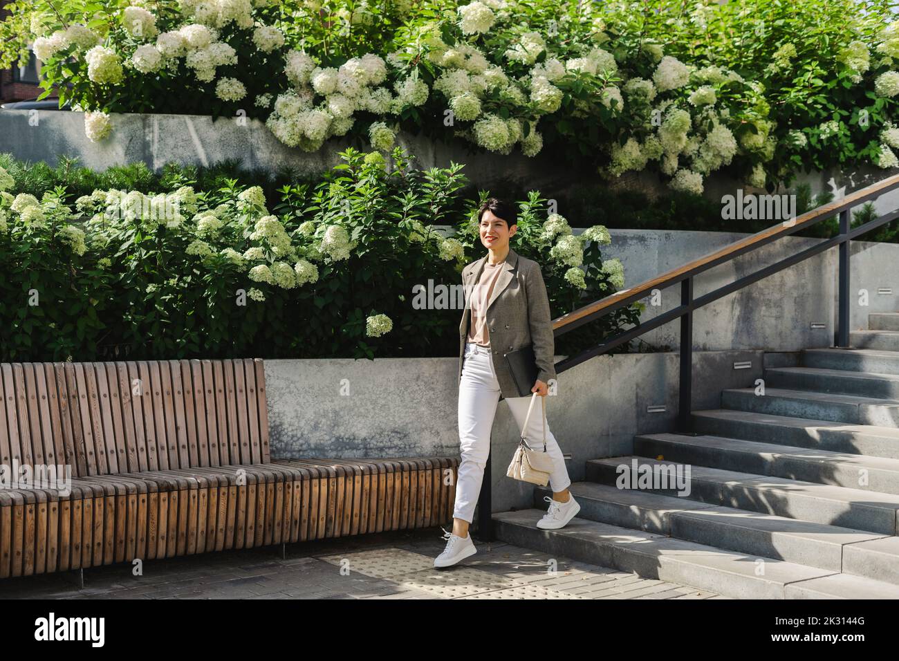 Smiling businesswoman with purse moving down from staircase on sunny day Stock Photo