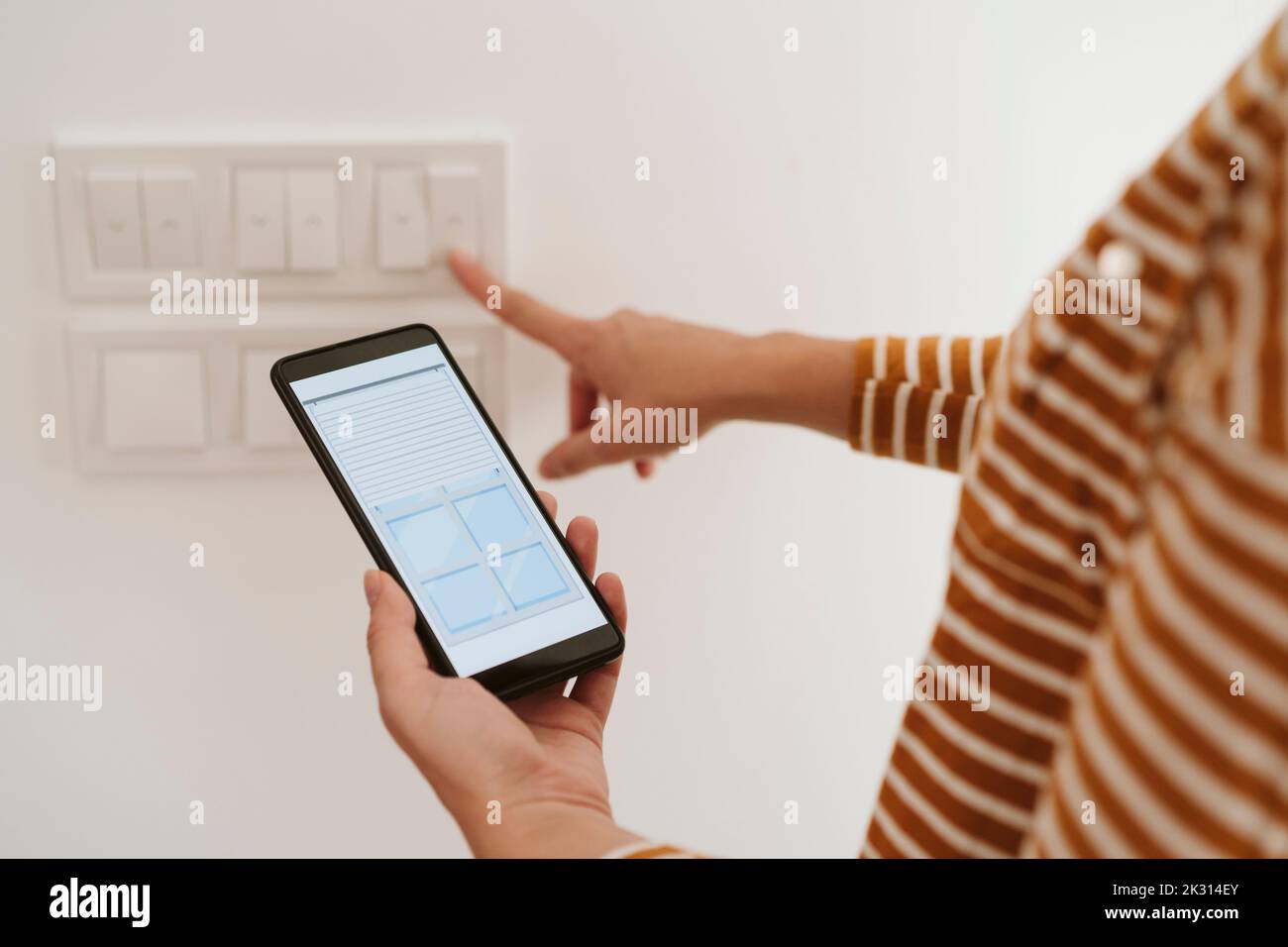 Woman touching switch for blinds while checking mobile phone app Stock Photo