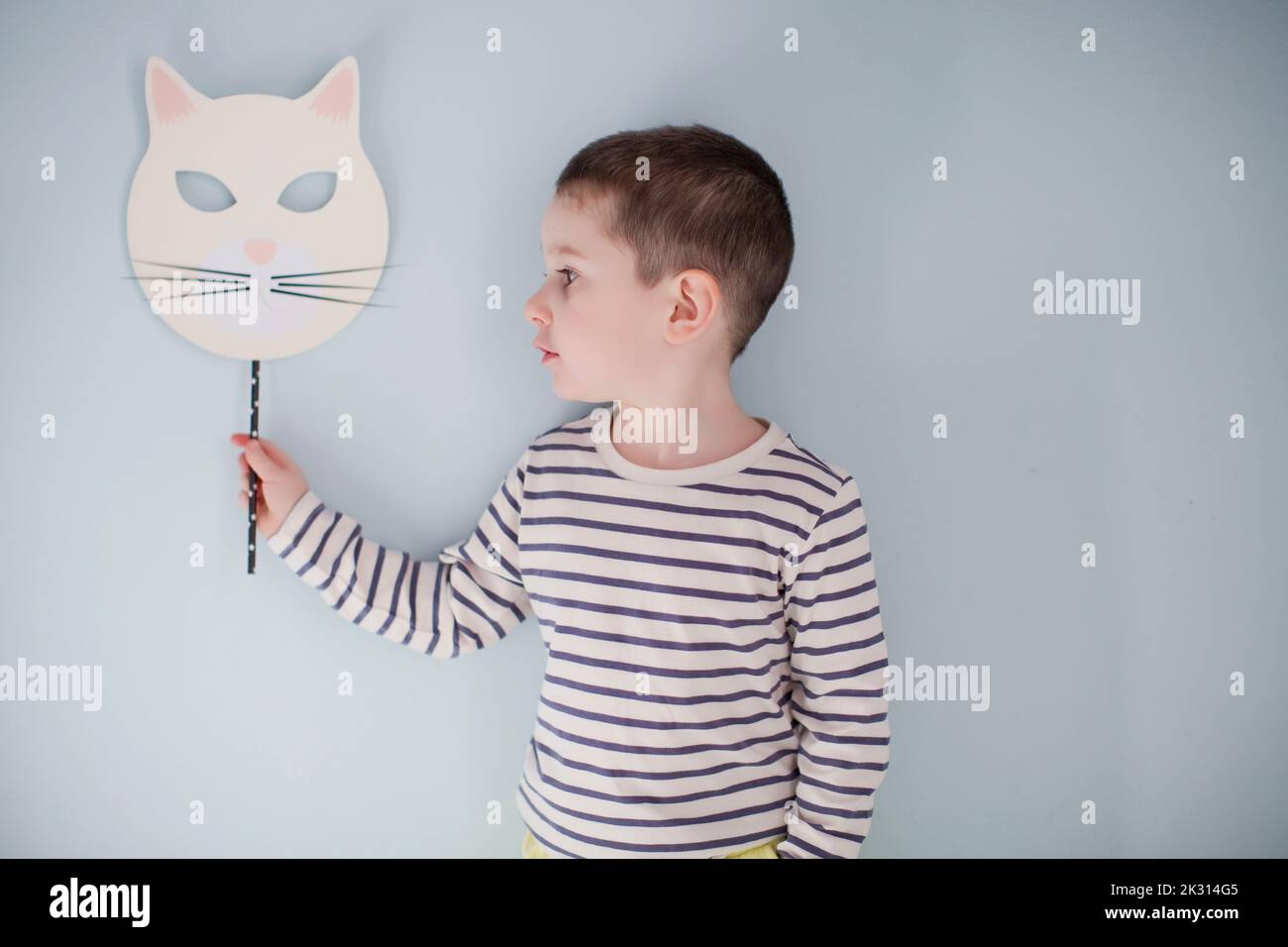 Boy standing with Halloween mask in front of gray wall Stock Photo