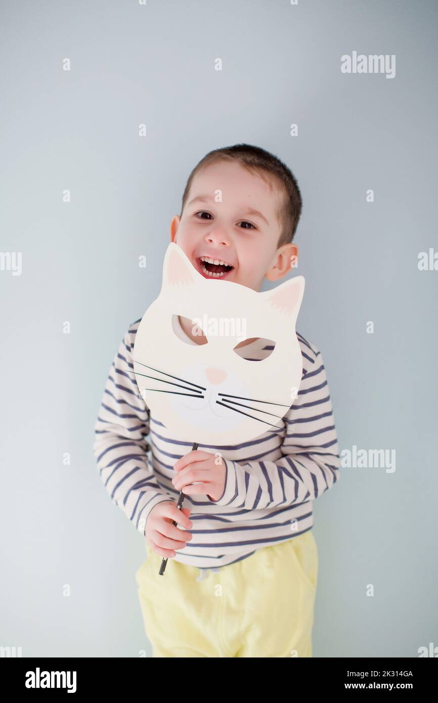 Happy cute boy standing with handmade Halloween mask in front of gray