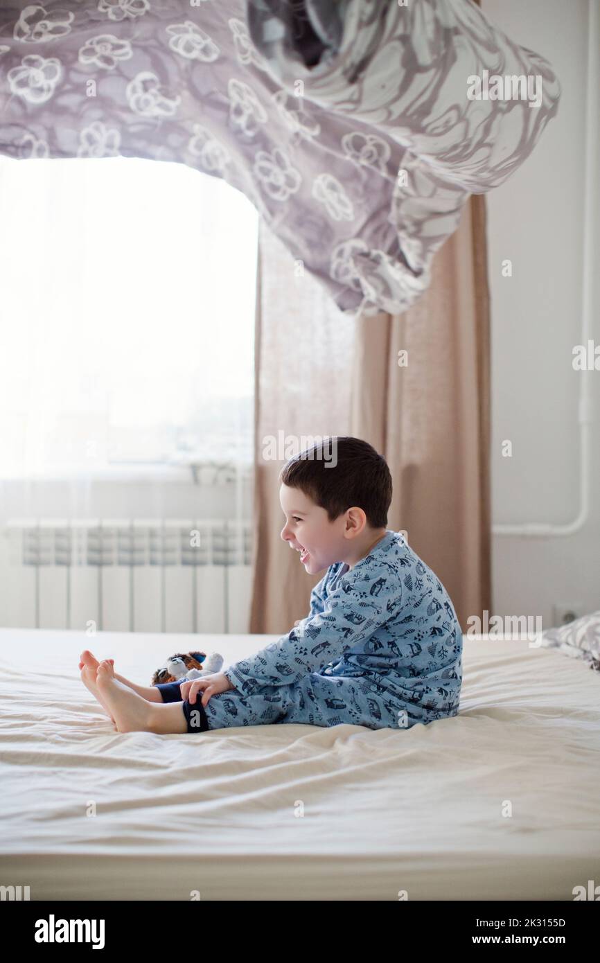 Playful boy sitting on bed under blanket in mid-air Stock Photo
