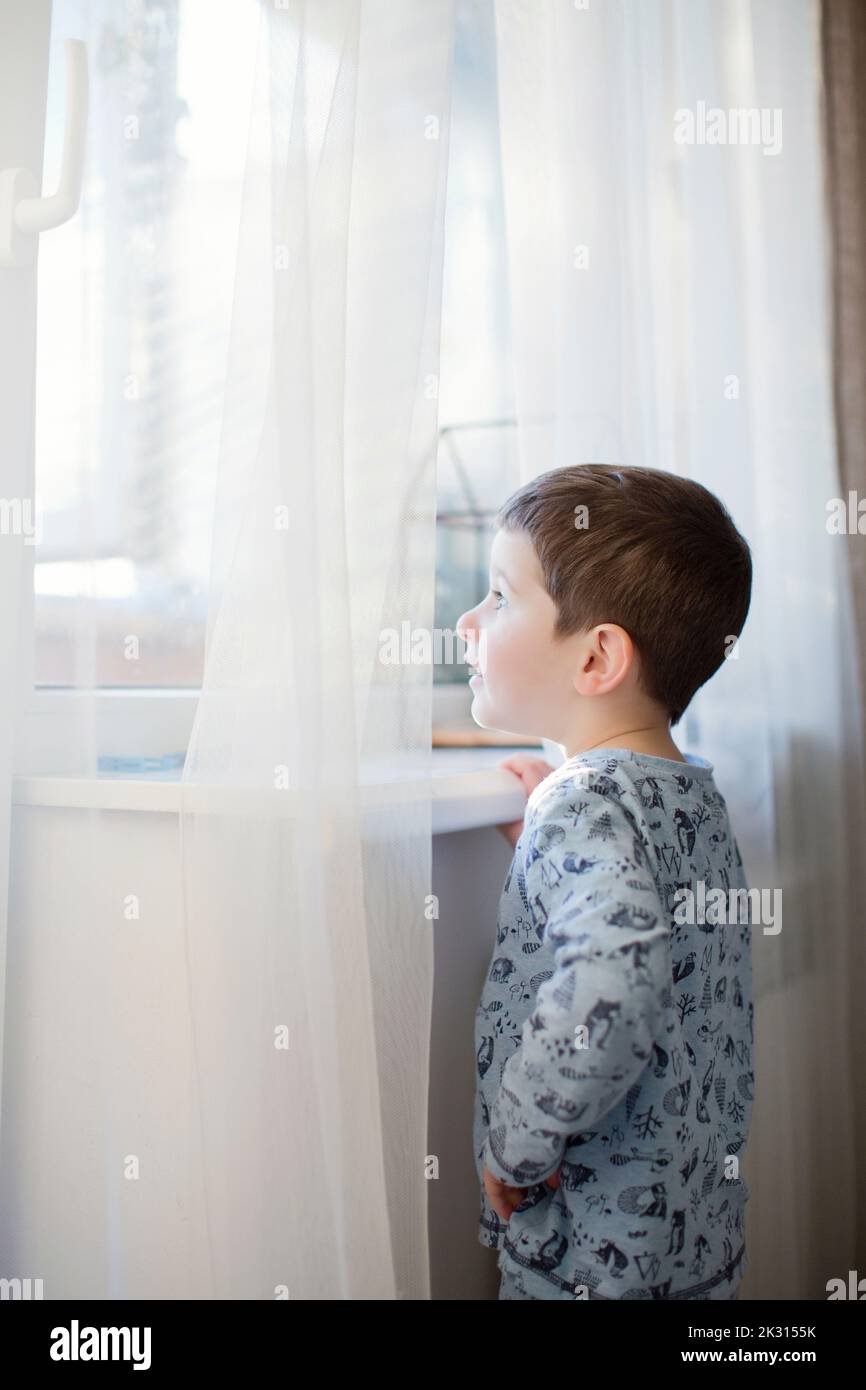 Boy wearing pajamas looking through window at home Stock Photo