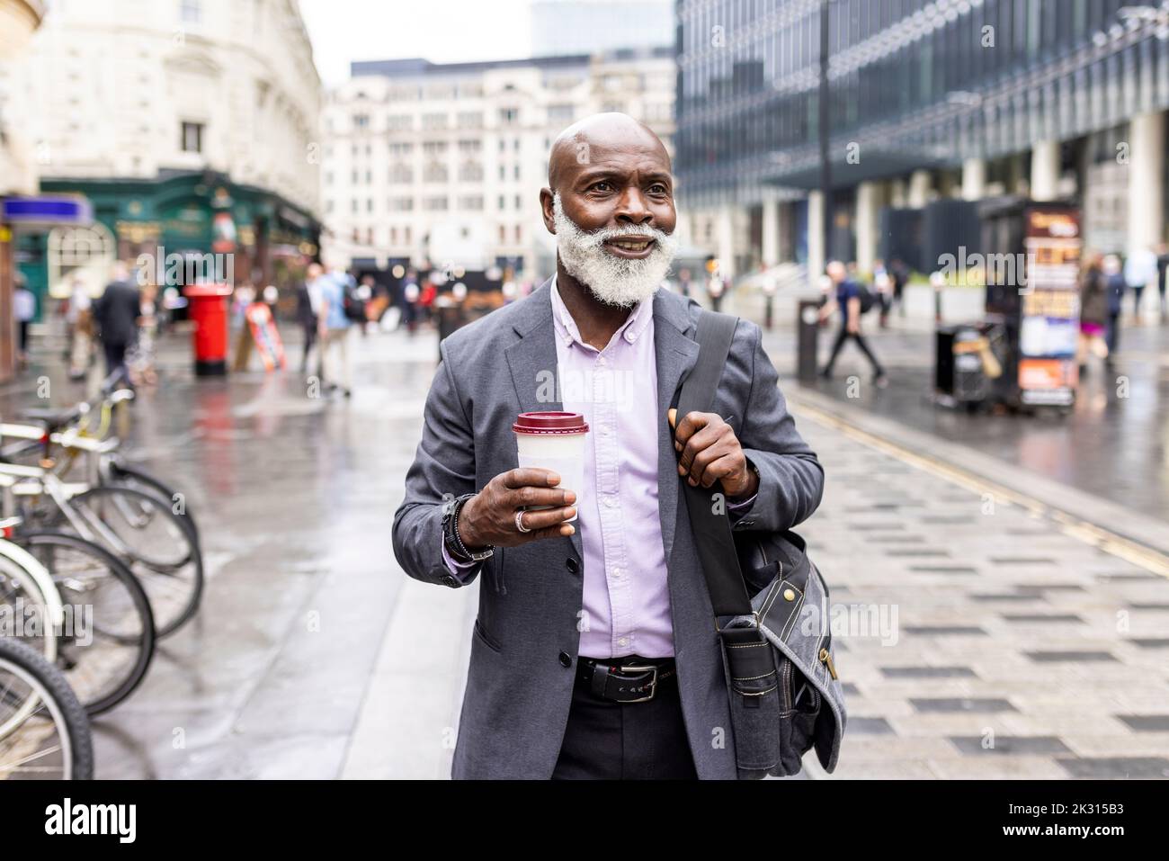 Smiling senior businessman with disposable coffee cup on footpath Stock Photo
