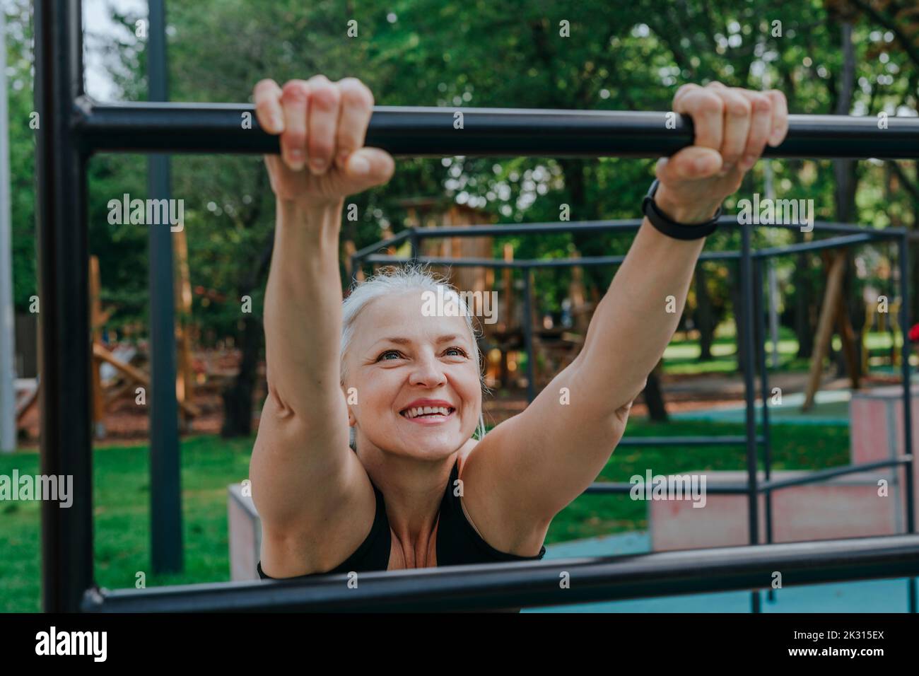 Happy mature woman stretching on bars in playground Stock Photo
