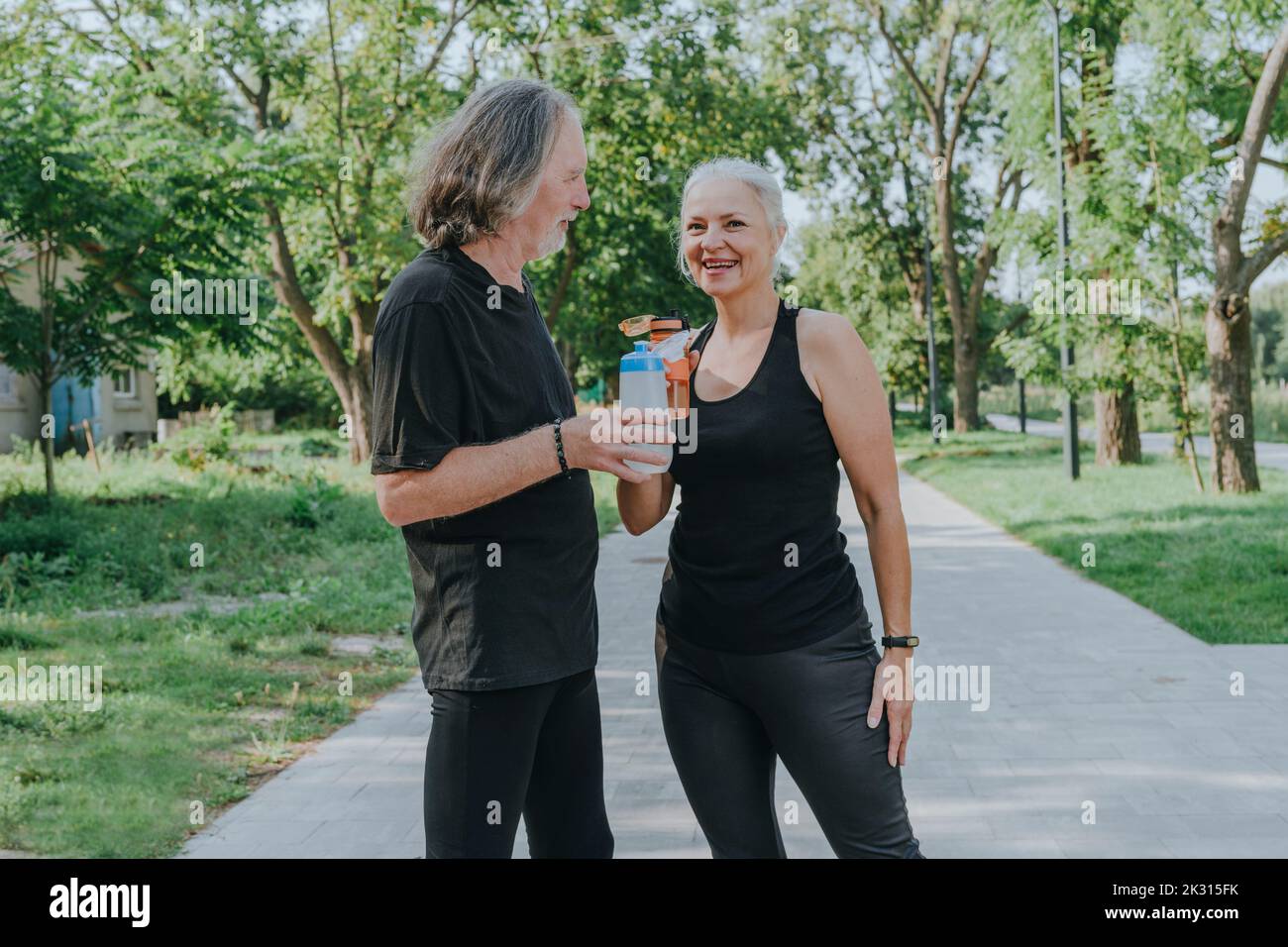 Woman and senior man drinking water in park Stock Photo