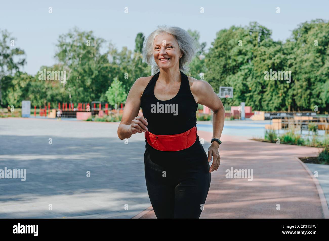 Happy mature woman with waistband jogging in park Stock Photo