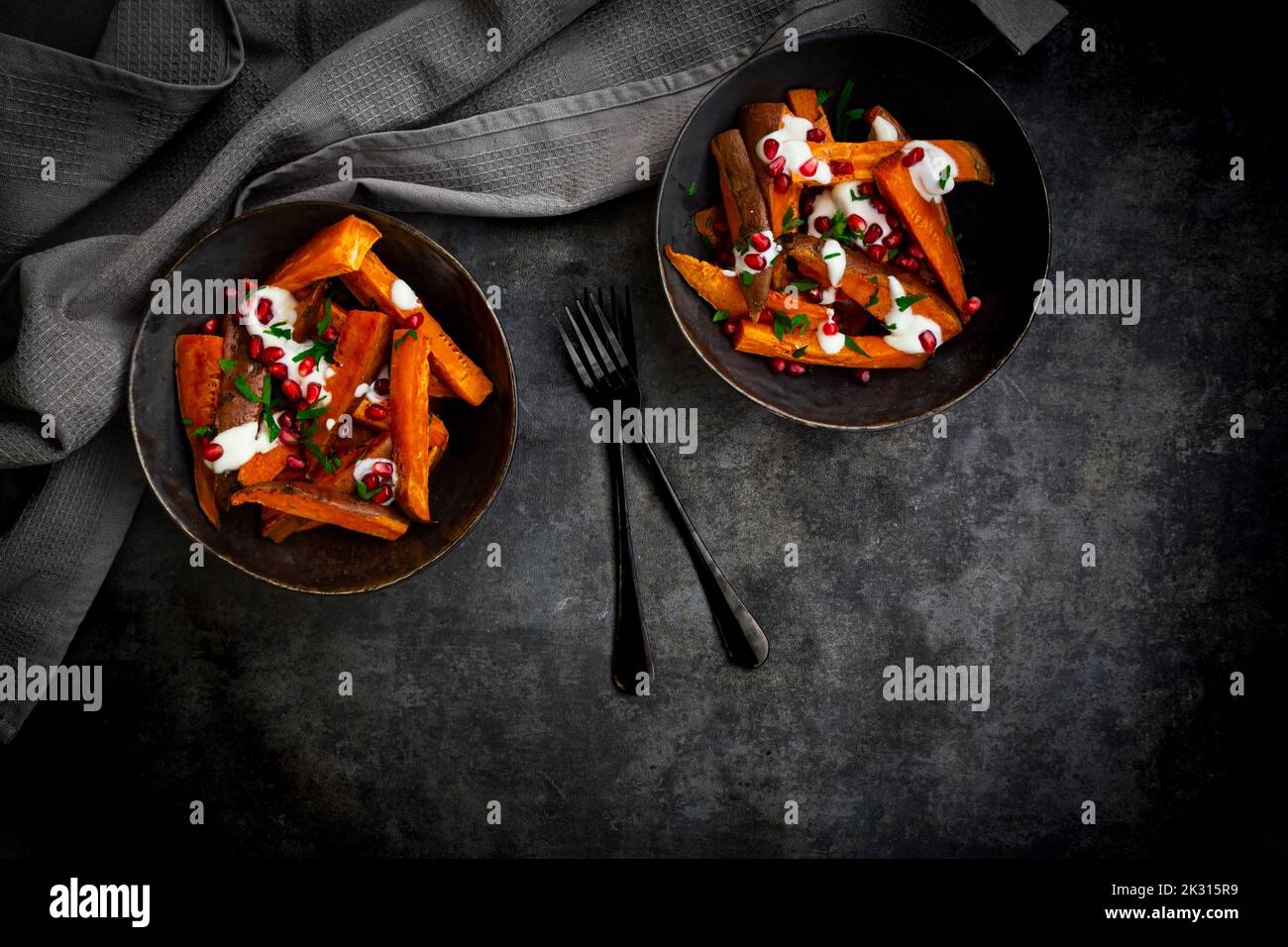 Studio shot of two bowls of sweet potatoes with parsley, pomegranate seeds and yogurt sauce Stock Photo