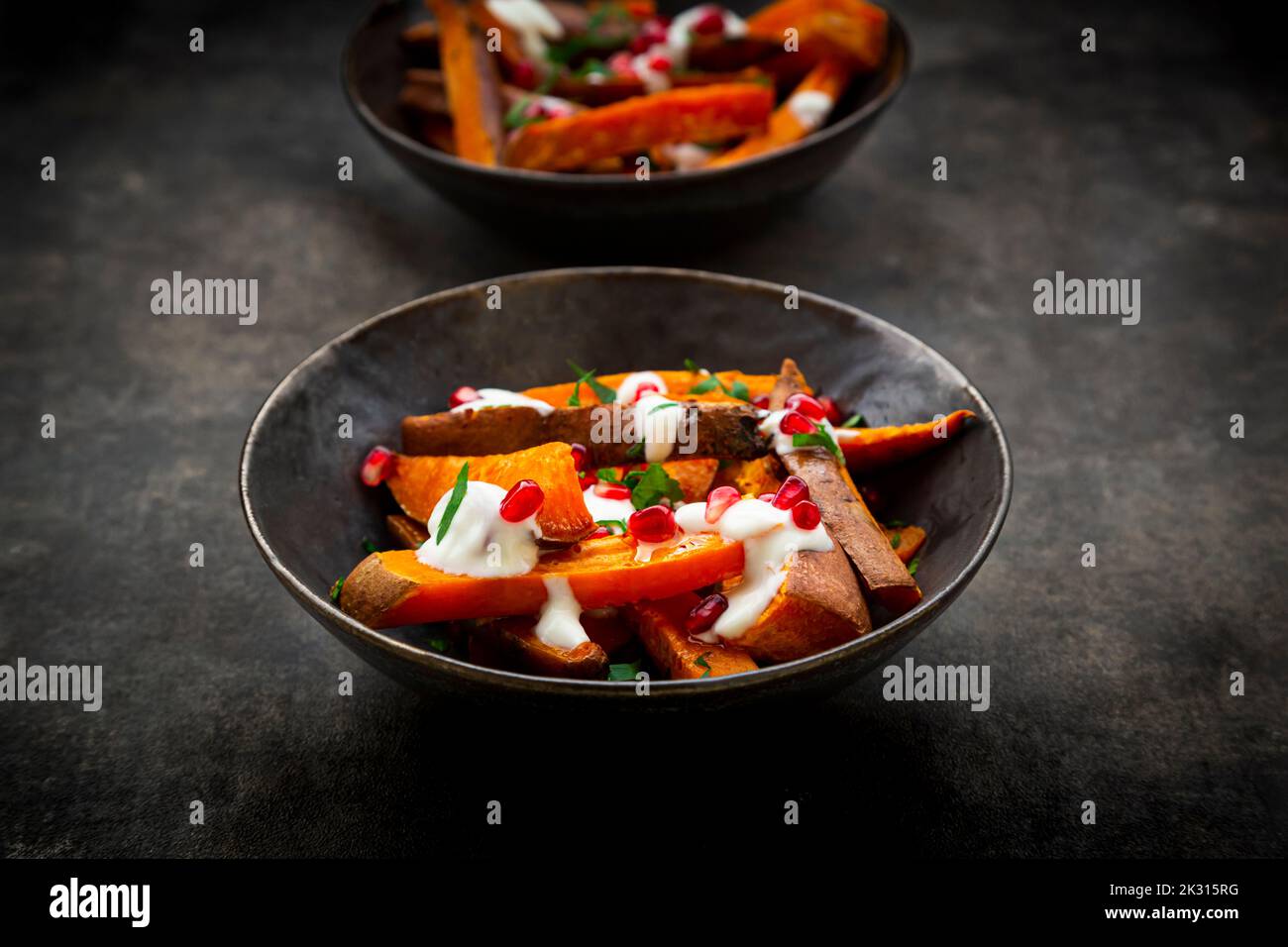 Studio shot of two bowls of sweet potatoes with parsley, pomegranate seeds and yogurt sauce Stock Photo