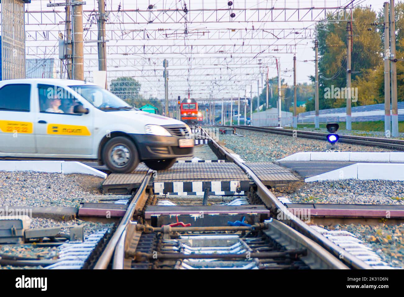 Kemerovo, Russia - September 01, 2022. A hurrying taxi car dangerously crosses a railway crossing in front of an approaching train, selective focus Stock Photo