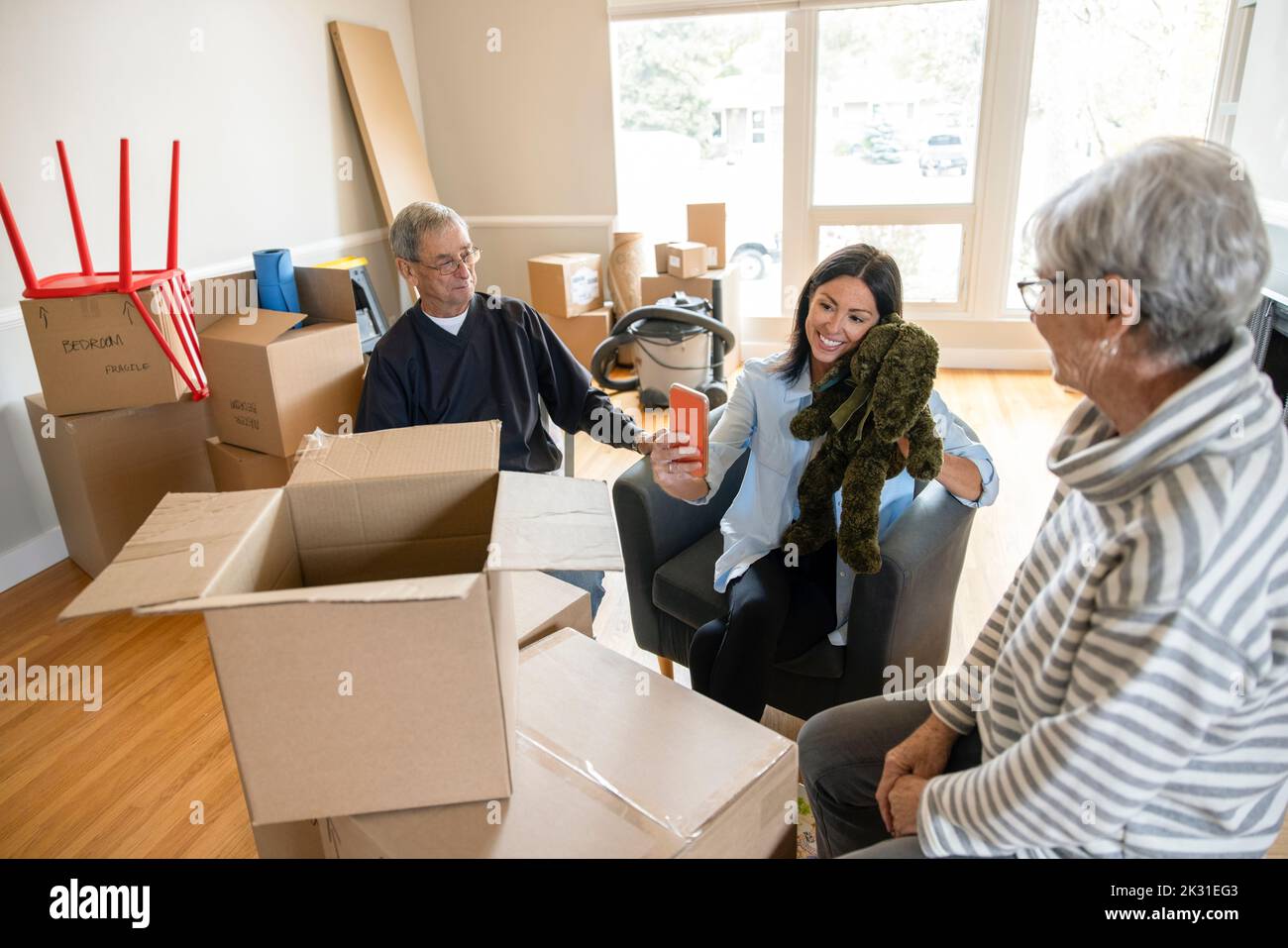 Senior parents watching daughter unpack old stuffed animal in new home Stock Photo
