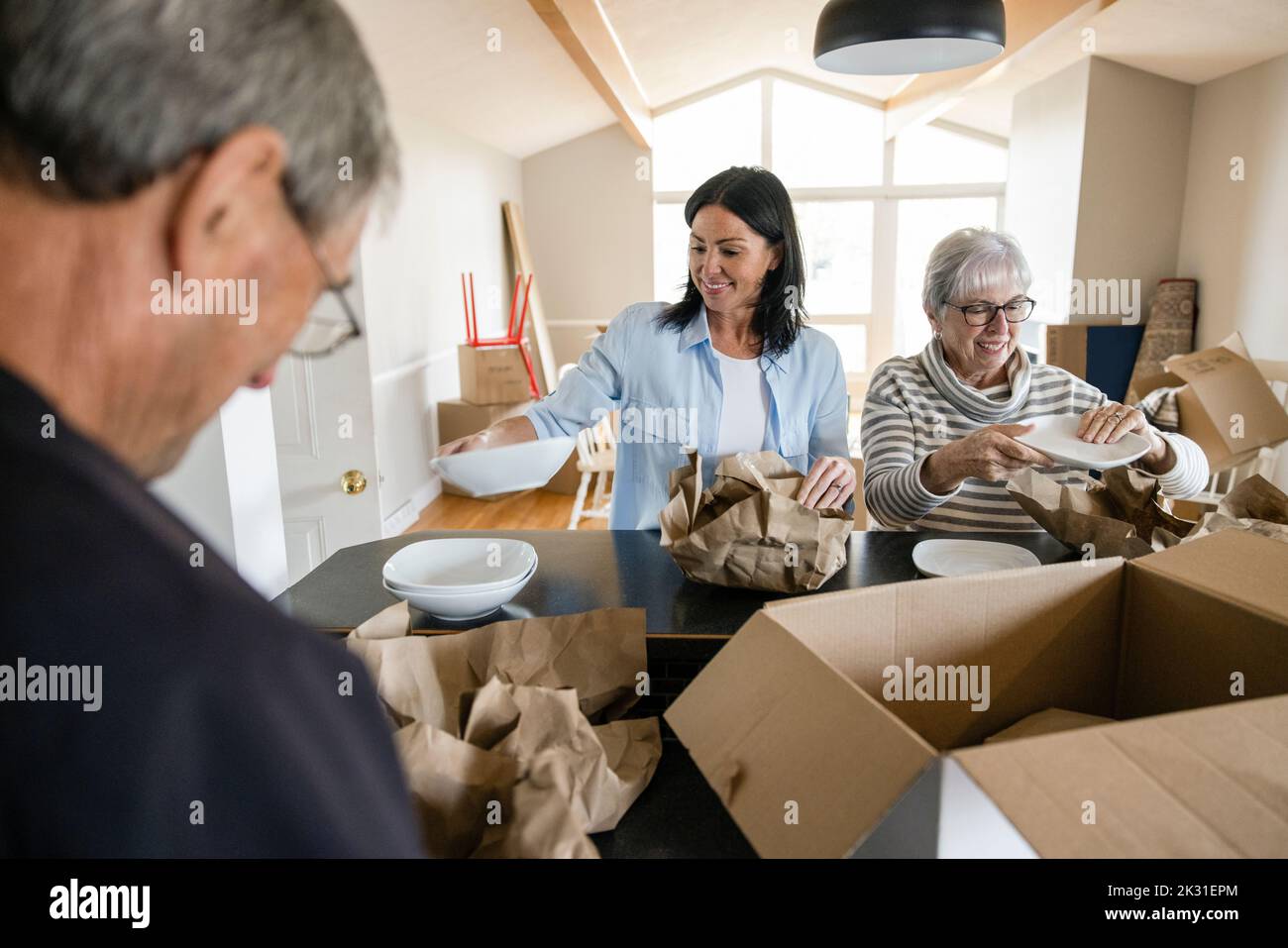 Happy daughter helping senior parents unpack dishes in new home Stock Photo