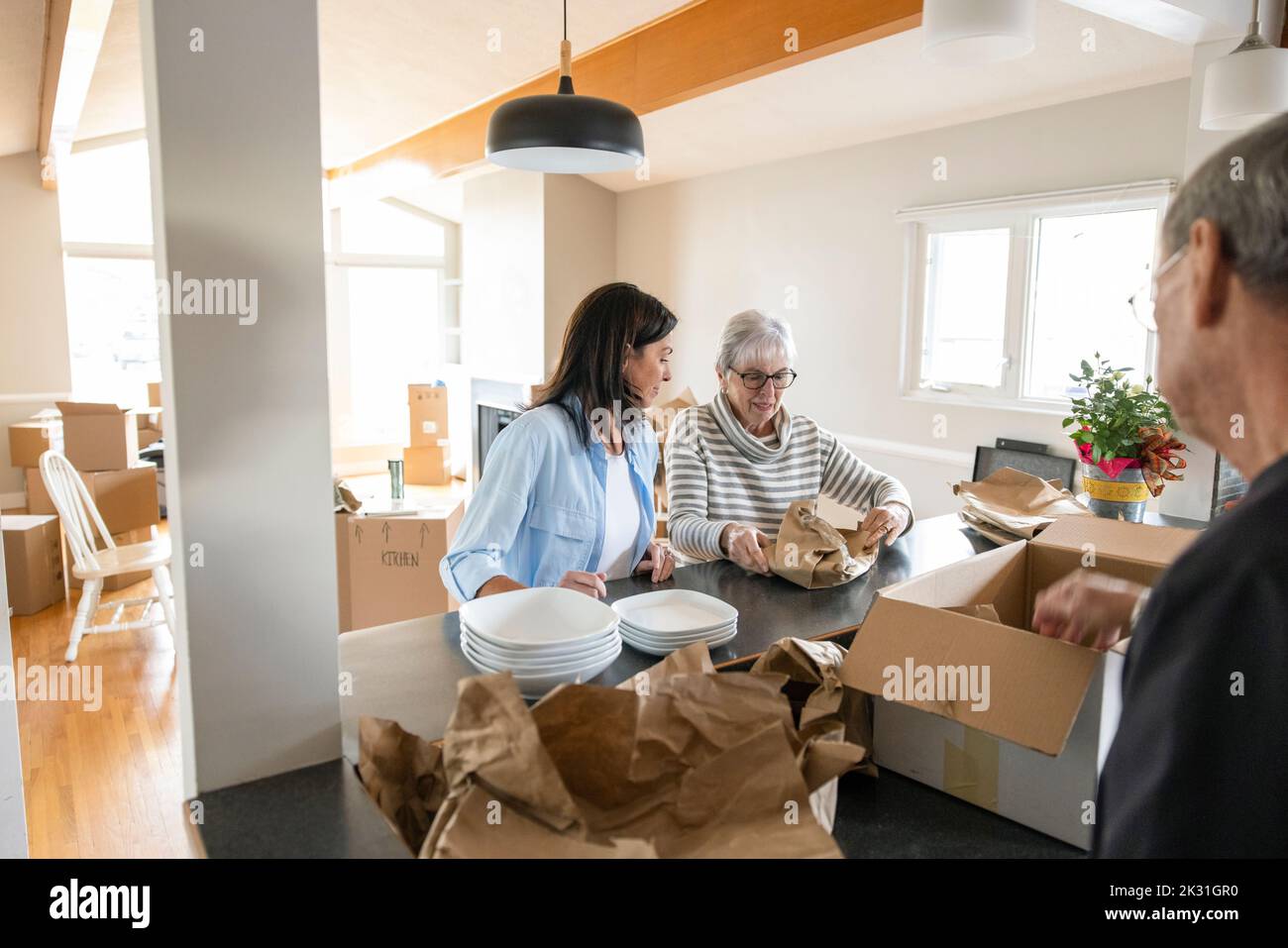 Daughter helping senior parents unpack dishes in new home Stock Photo