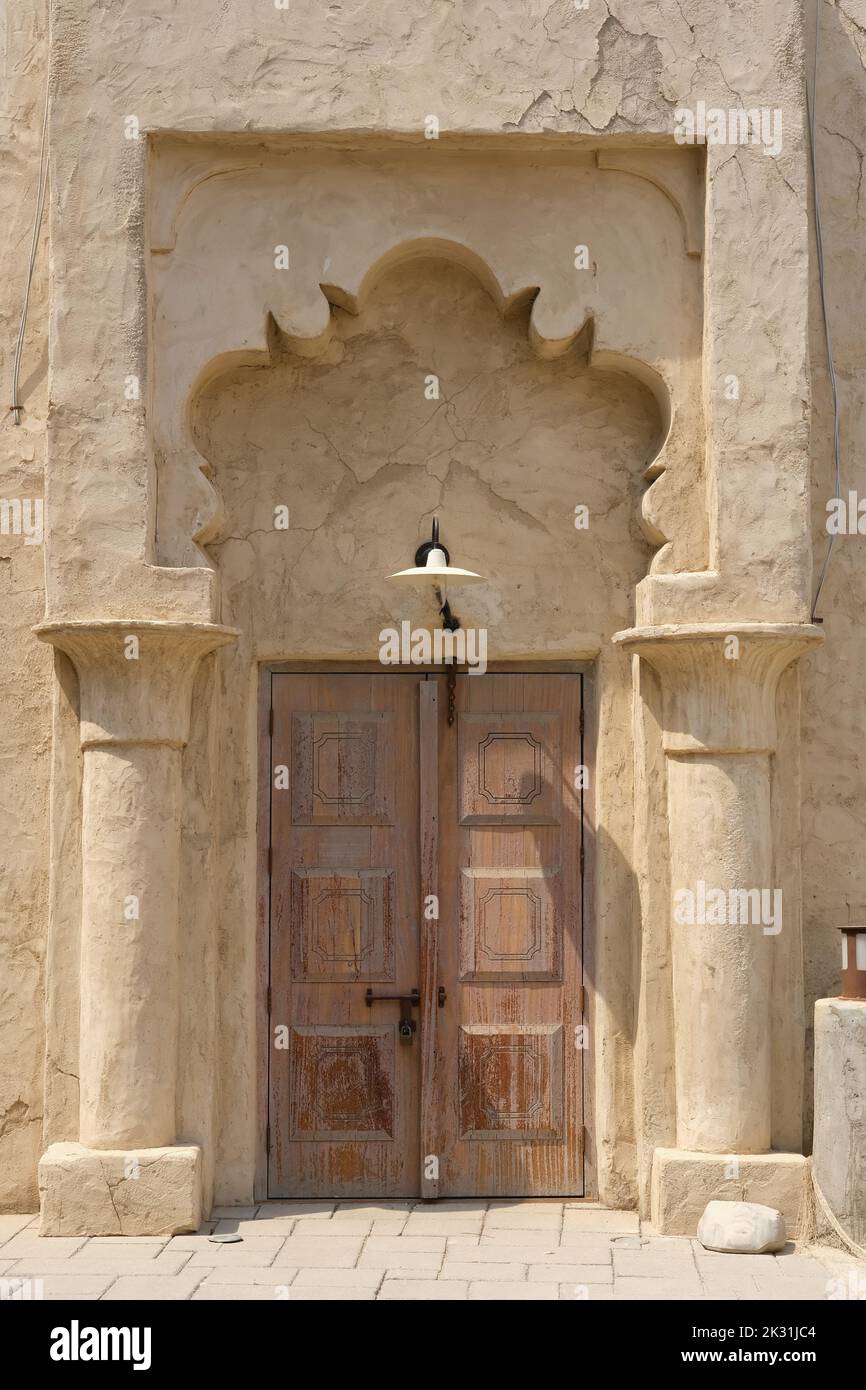 Vintage entrance to the oriental house with worn wooden closed doors decorated with carved sandstone columns and arch.  Stock Photo