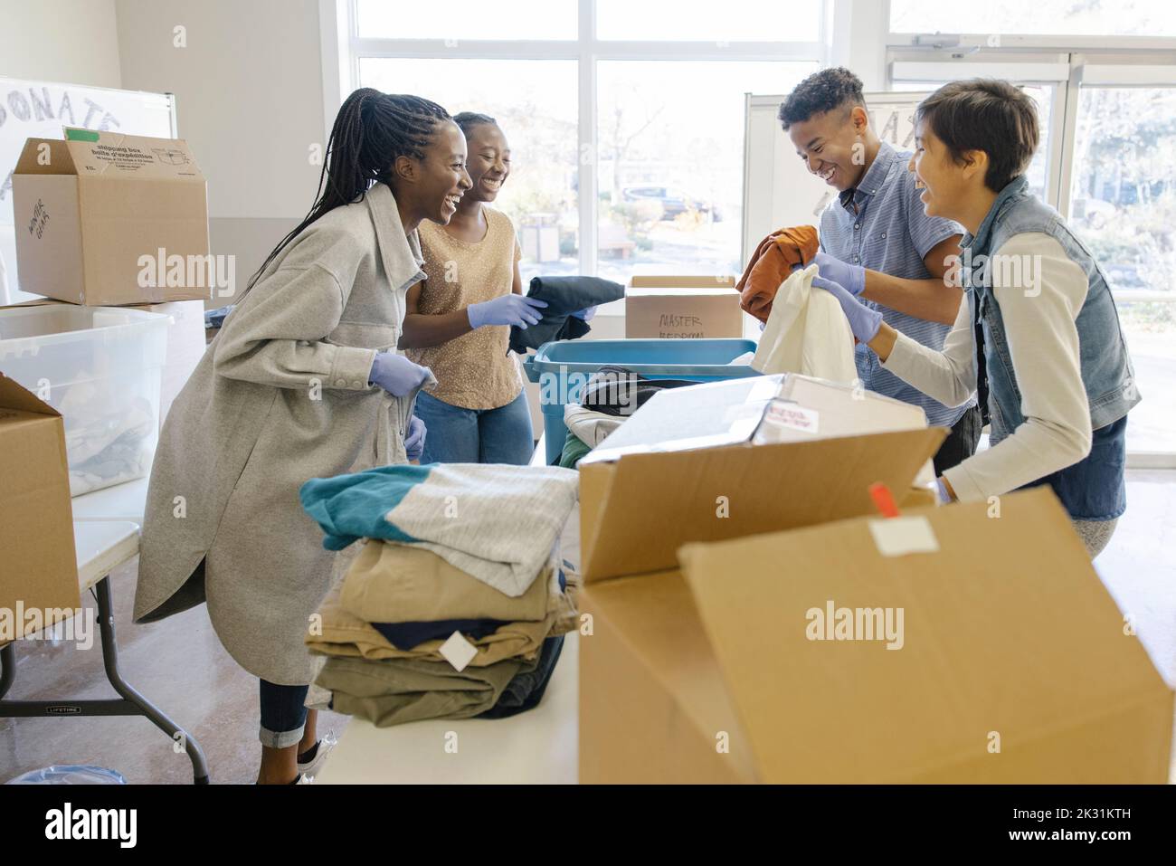 Happy teenage volunteers sorting clothing donation in community center
