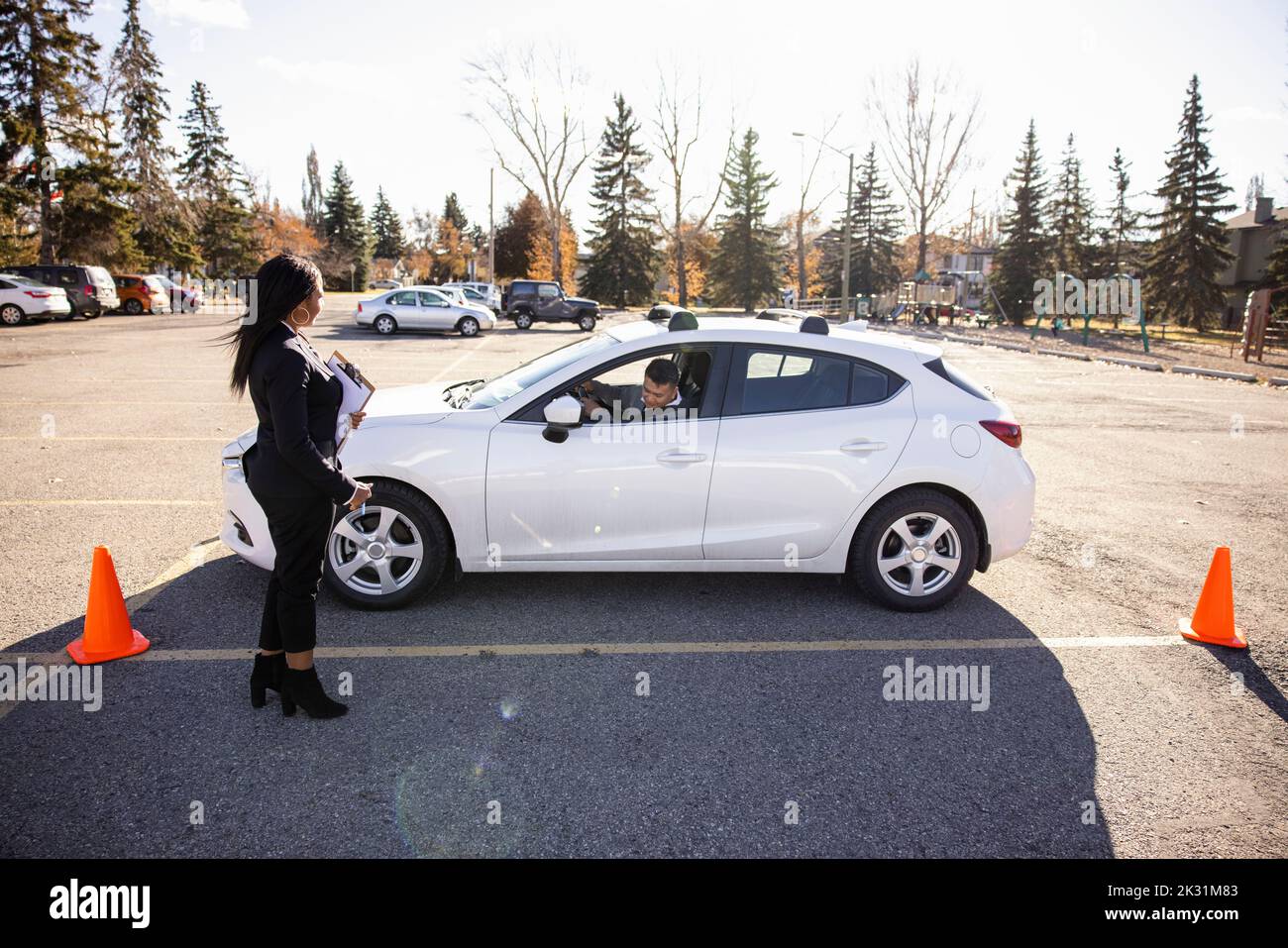 Driving instructor watching student park car in sunny parking lot Stock