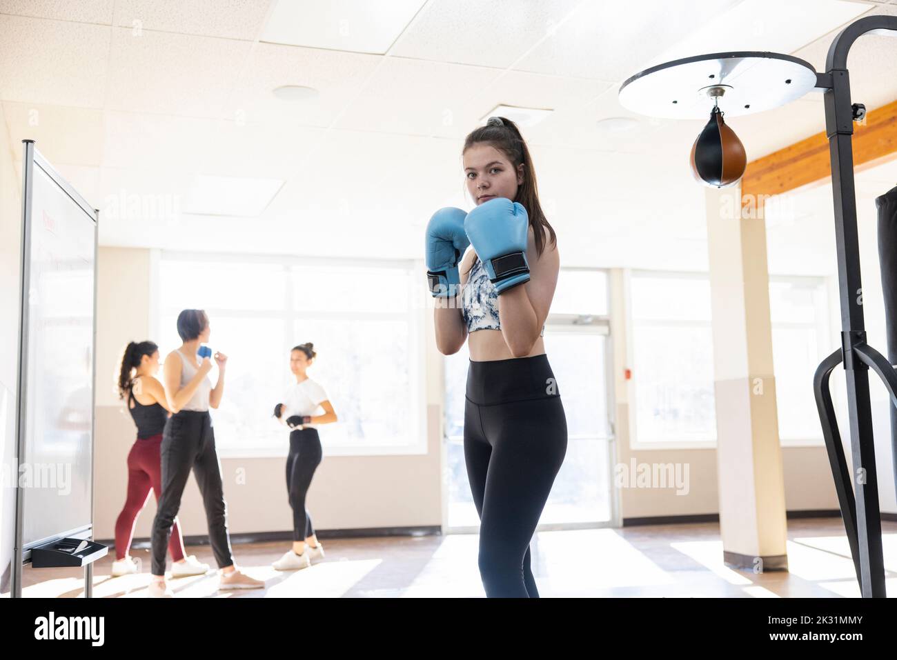 Portrait confident teen girl with boxing gloves in fighting stance
