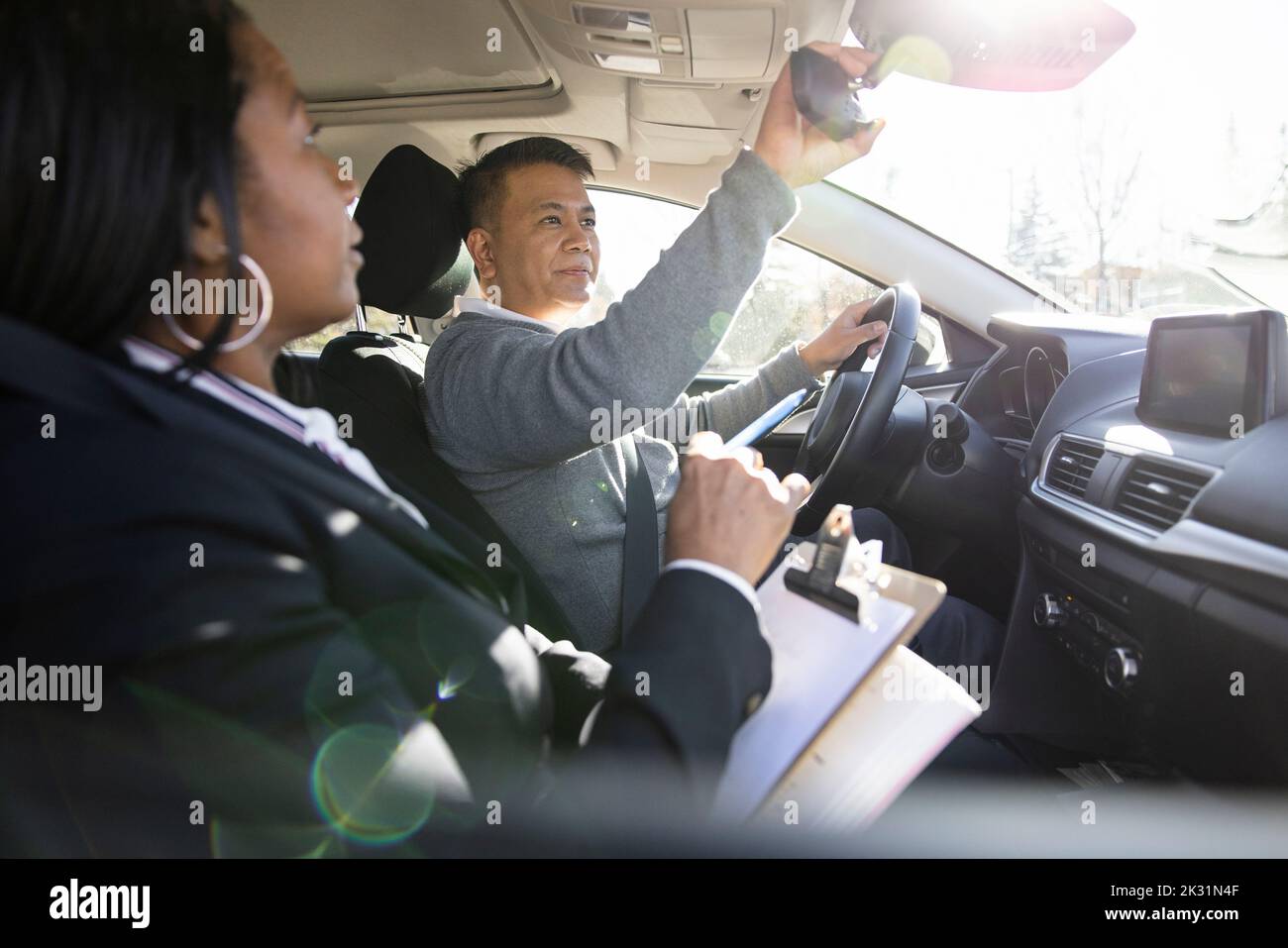 Driving instructor and student adjusting rear view mirror in sunny car