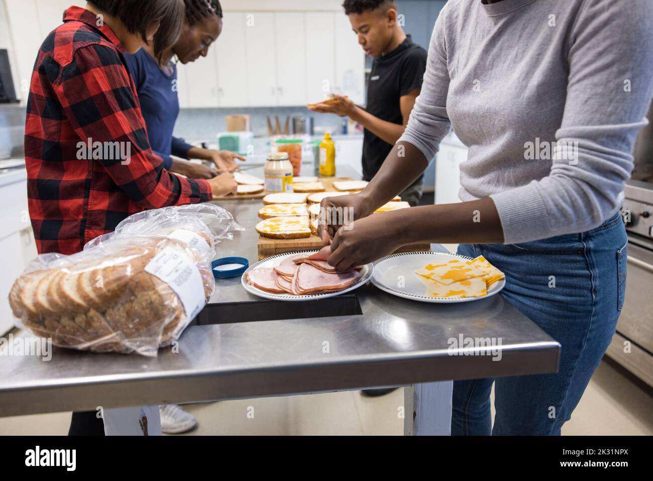 Volunteers making ham sandwiches in community center kitchen Stock
