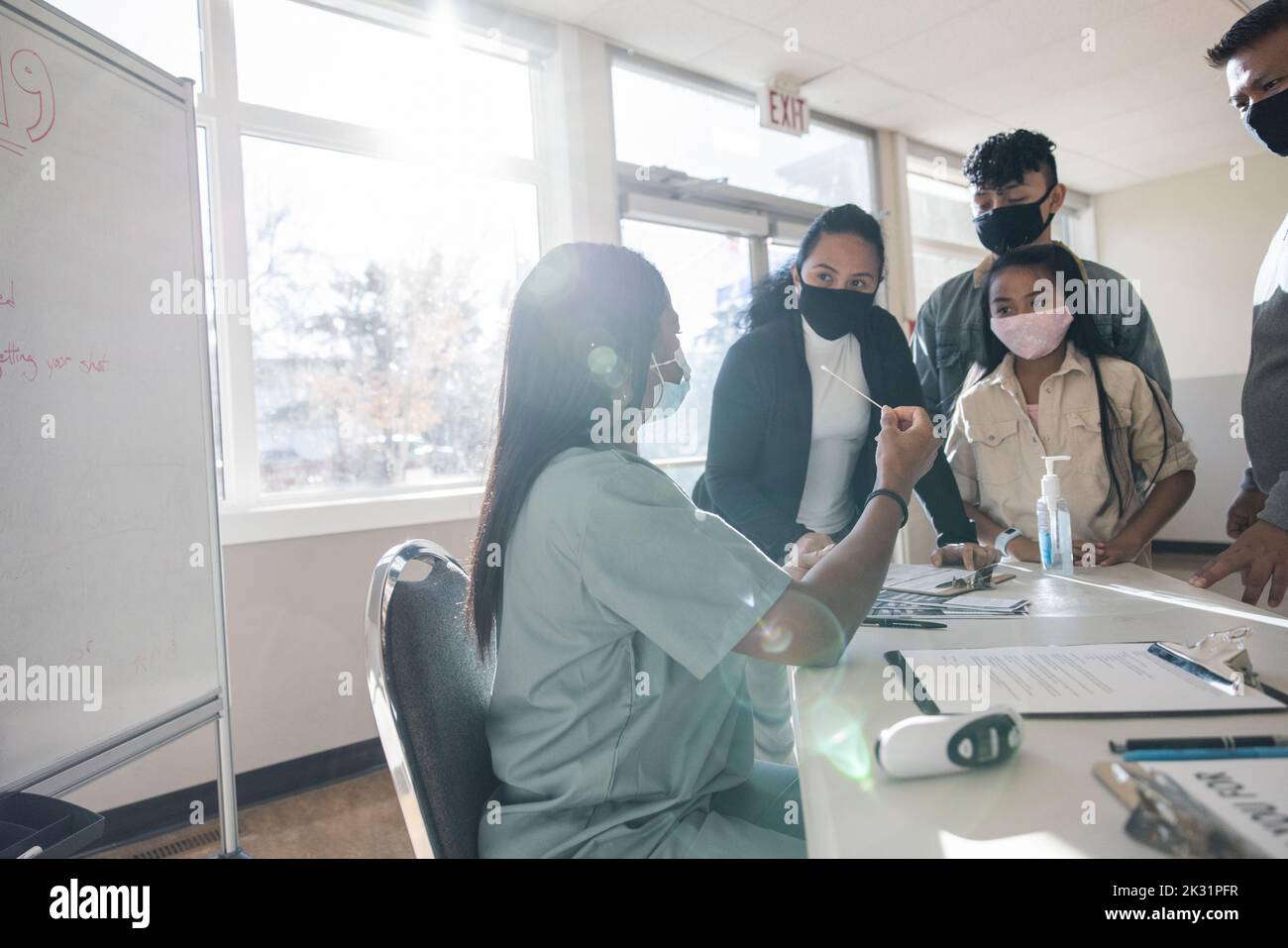 Nurse in face mask explaining COVID-19 swab test to family in clinic Stock Photo