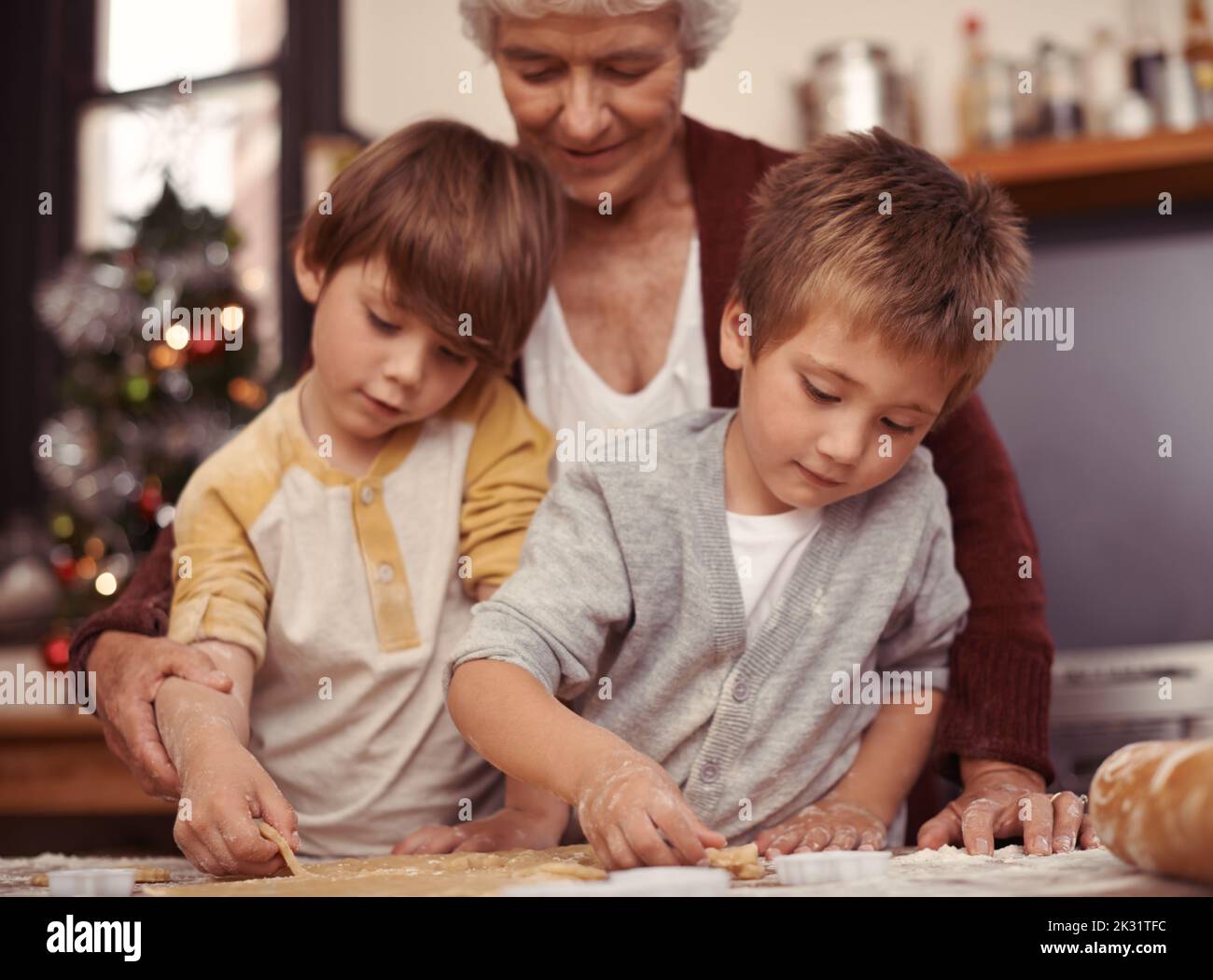 Messy but tasty. Two cute little boys baking with their grandmother in the kitchen. Stock Photo
