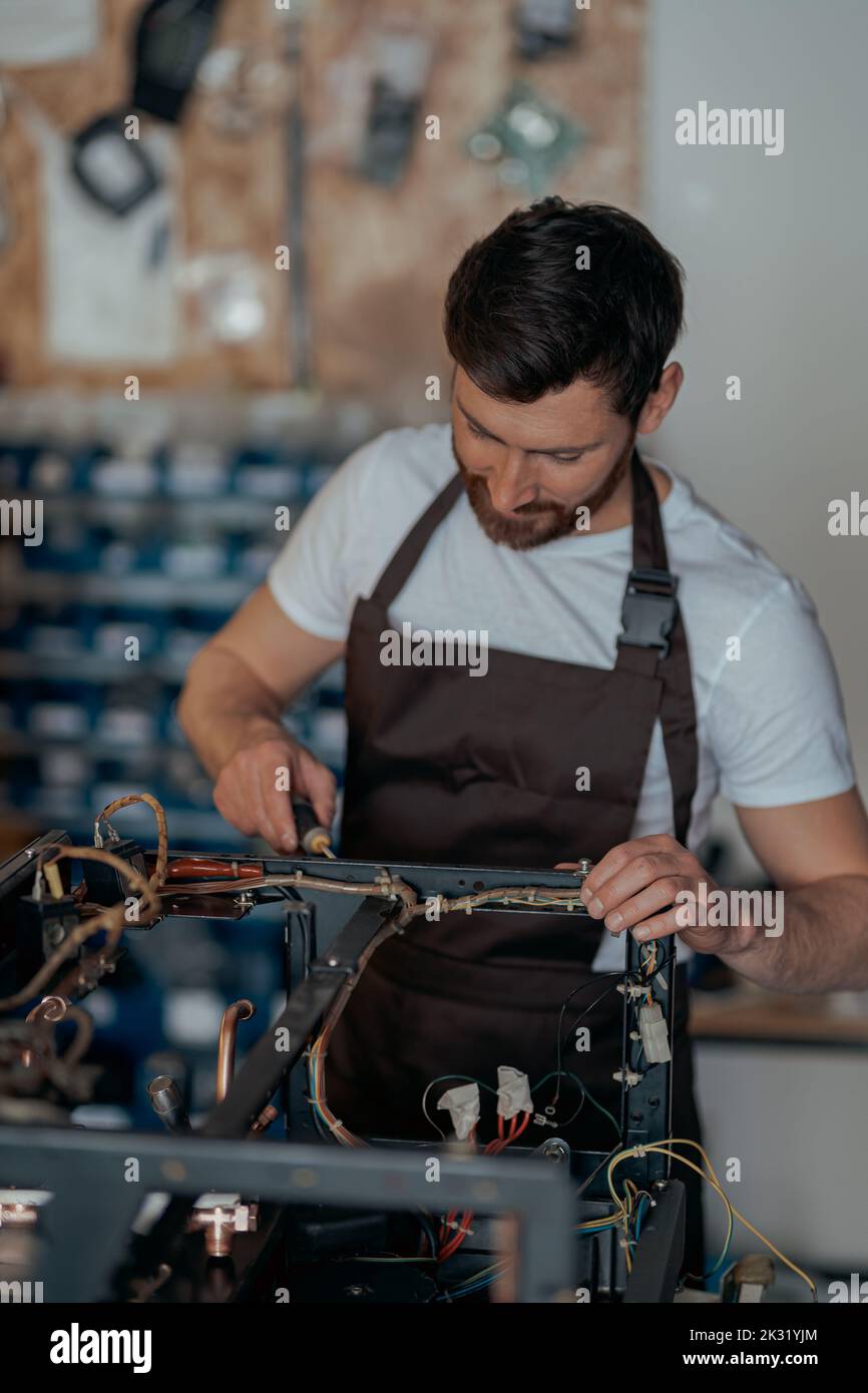Smiling young worker repairing coffee machine in a workshop Stock Photo