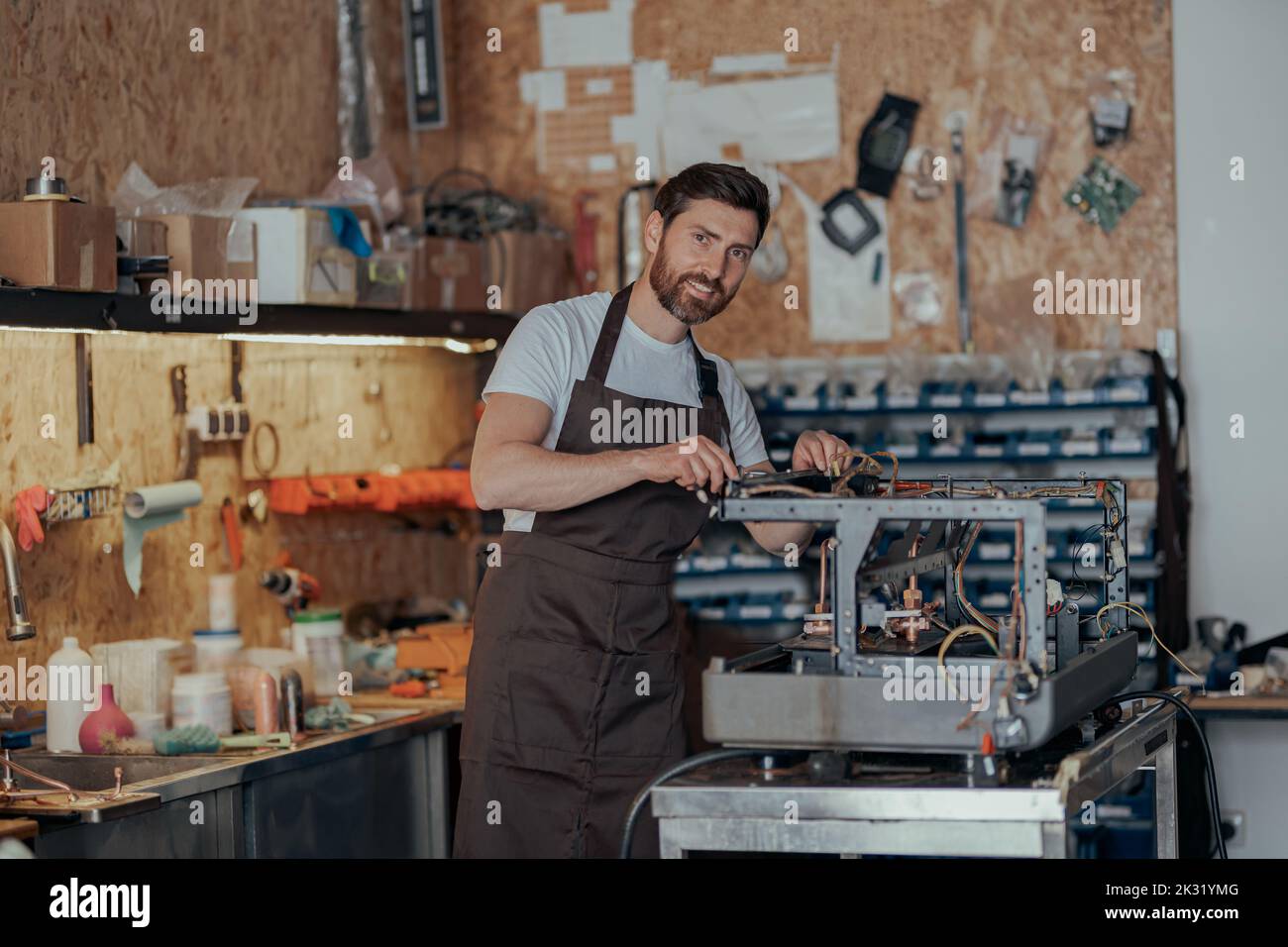 Portrait of repairman in uniform with broken coffee machine in workshop Stock Photo
