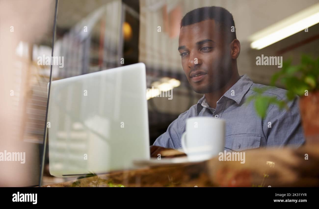 Business with the pleasure of coffee. a young african man using his laptop in a coffee shop. Stock Photo