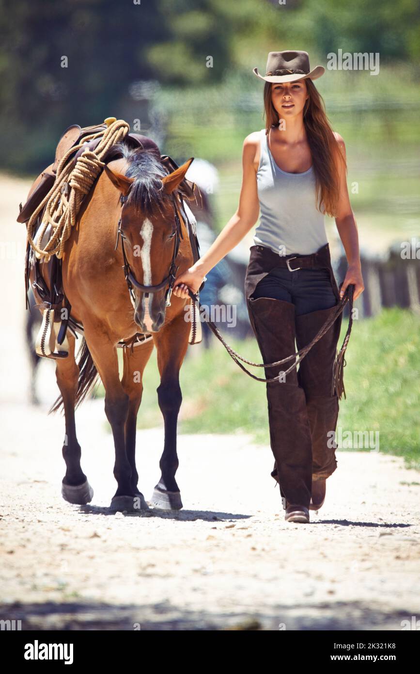Loving the outdoors. A beautiful young cowgirl leading her horse along a country road. Stock Photo
