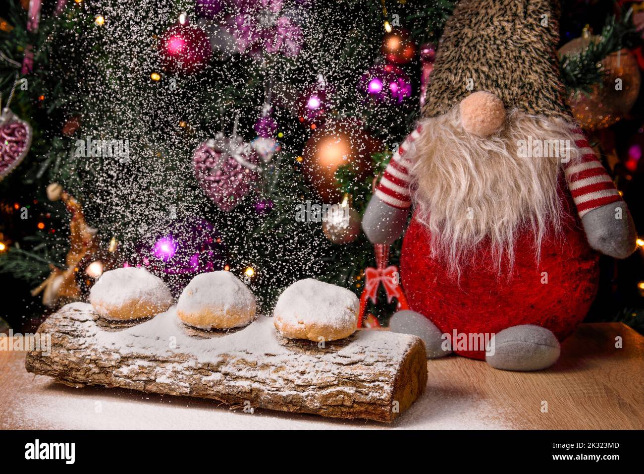 Cookies (kourabies)  with powdered sugar.  GreekTraditional Christmas sweet on a tree trunk, with a background of a Christmas tree and a toy gnome Stock Photo