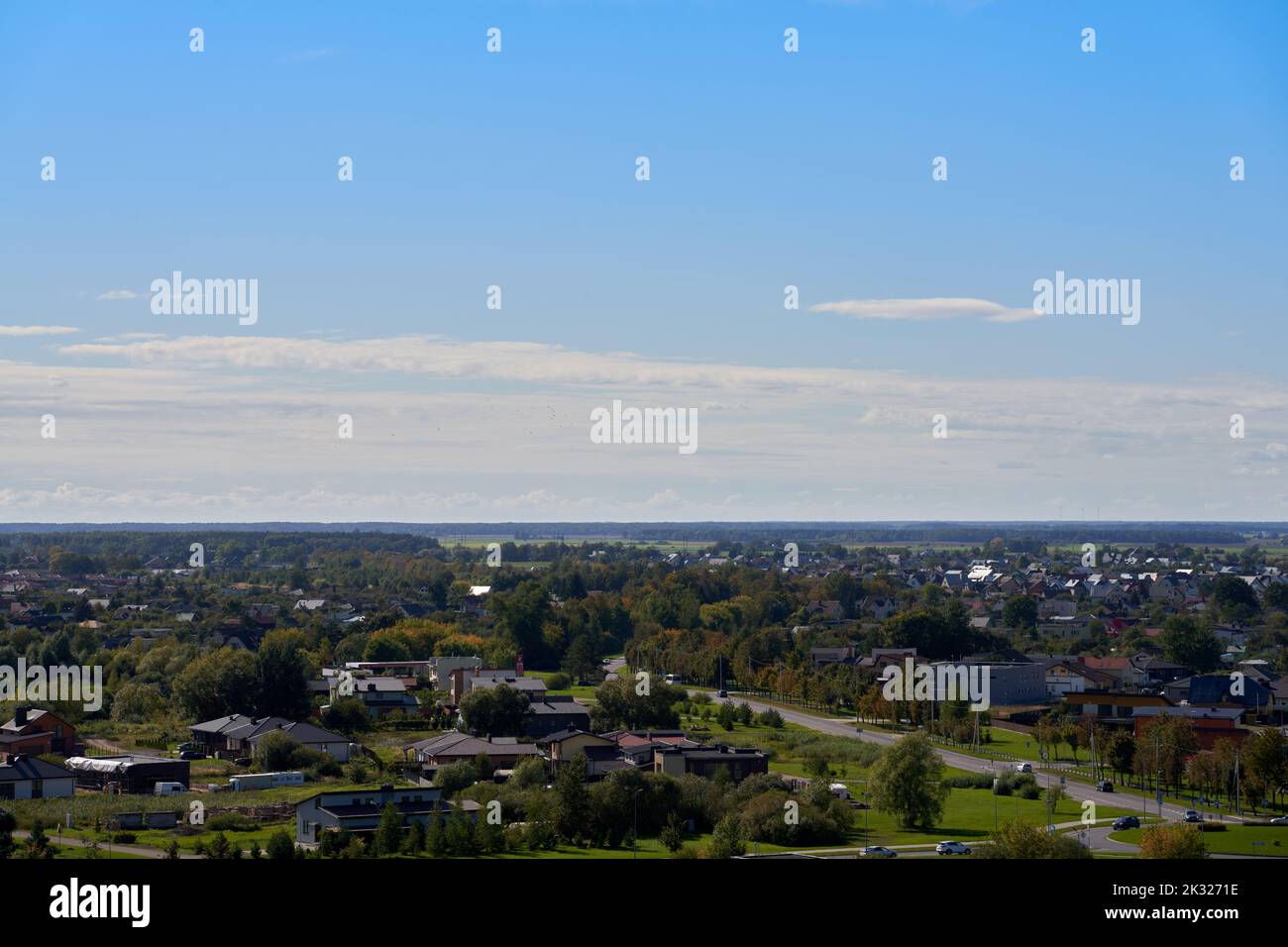 A high-angle shot of the city Panevezys suburbs with green trees, blue sky and clouds in the background Stock Photo