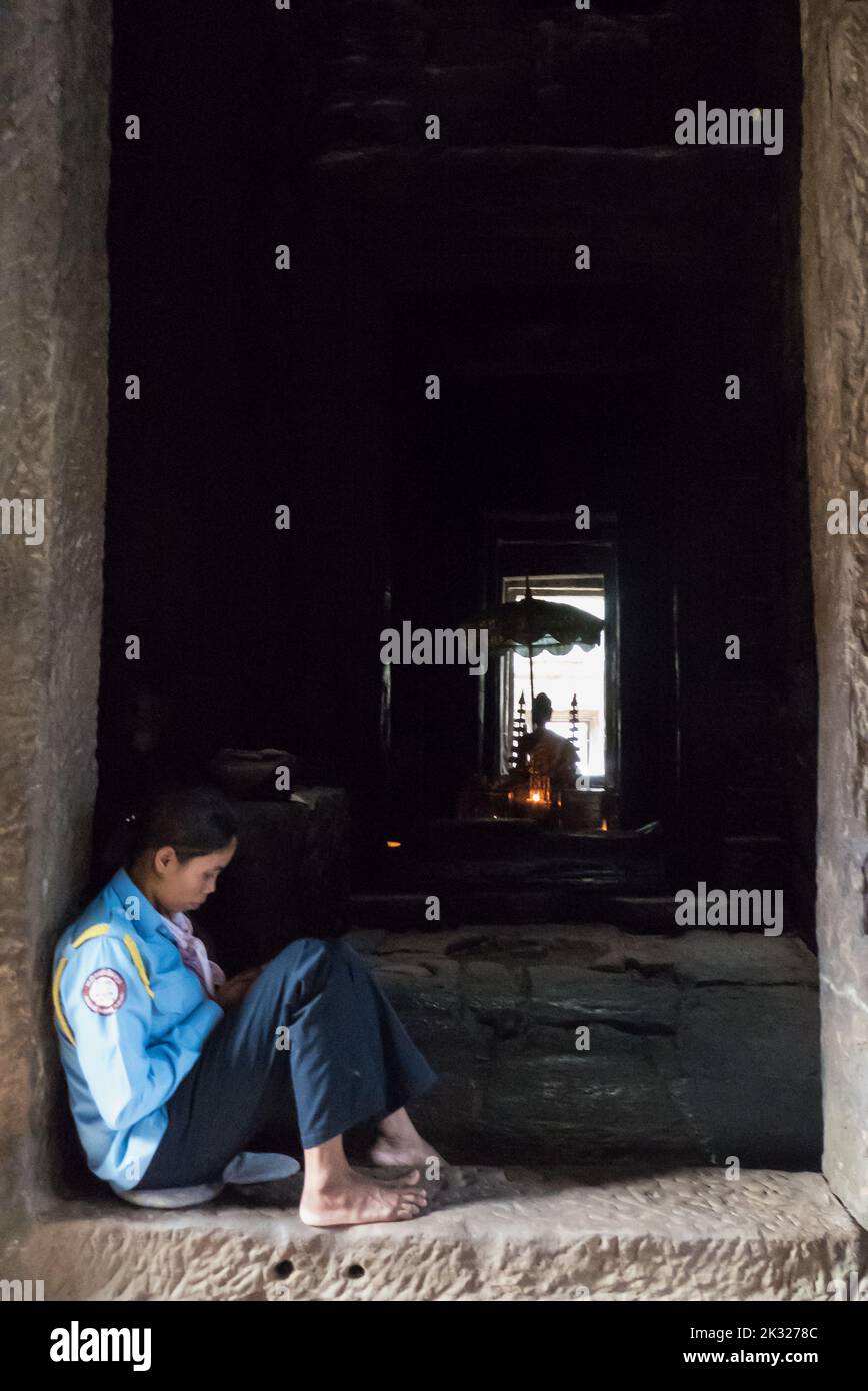 Local guide guards a Buddhist shrine within the inner sanctuary, Prasat Bayon, Angkor, Siem Reap, Cambodia Stock Photo