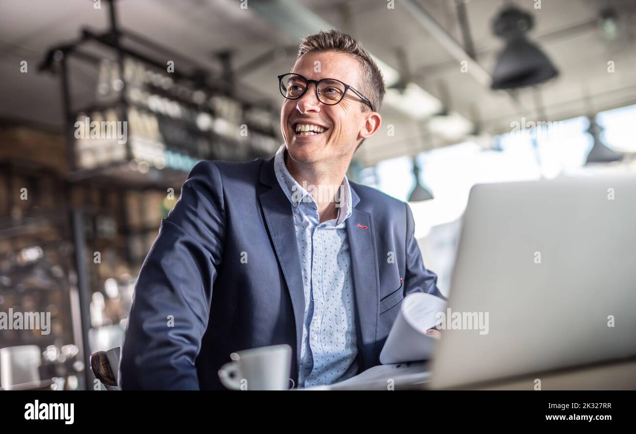 Entrepreneur smiles at the computer screen while having a coffee during a business break in a vintage restaurant. Stock Photo