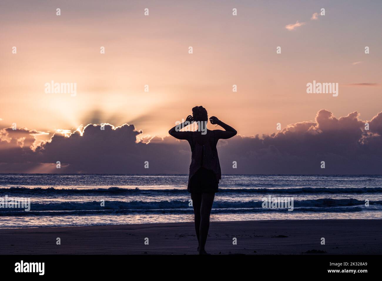 A silhouette of a woman standing at the beach enjoying the view of the ...