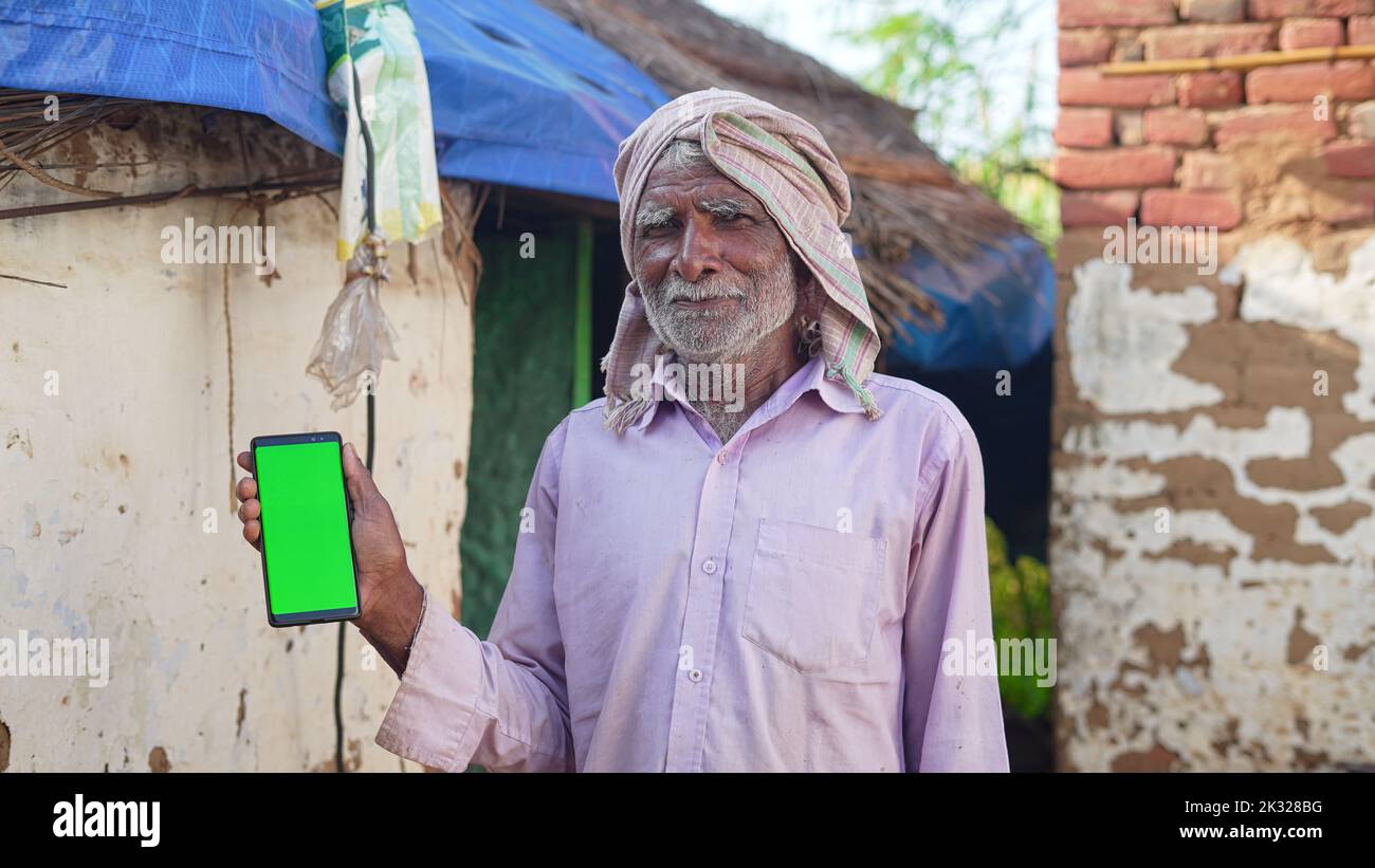 Old Asian man smiling and showing a green screen cell phone with rural village life concept background. Stock Photo