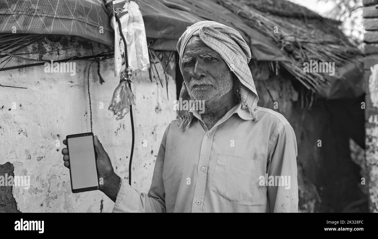 Indian old man holding a mobile phone and point towards it's screen. Mobile phone with a green screen for mockup. Stock Photo