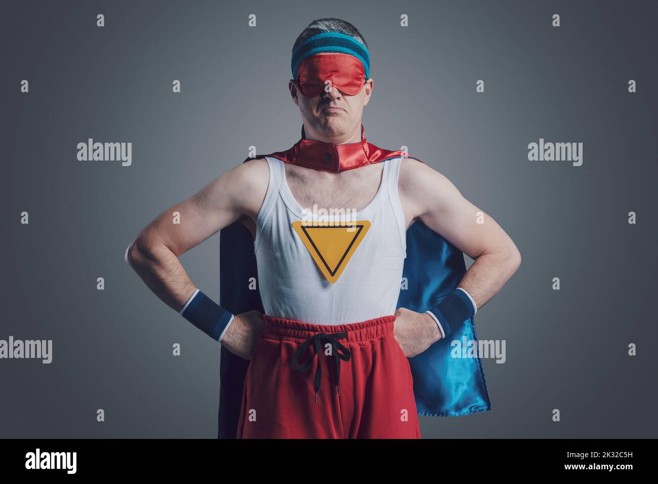 Funny confident superhero posing with arms akimbo, he is wearing a sleep mask over his eyes Stock Photo