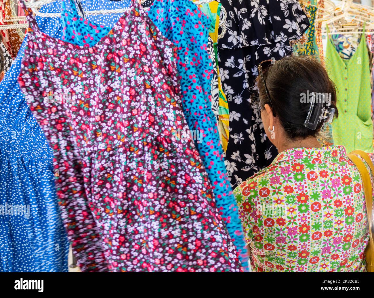 Woman in her 50s looking at colorful dresses to buy at a street market one summer morning in Mallorca (Spain) Stock Photo