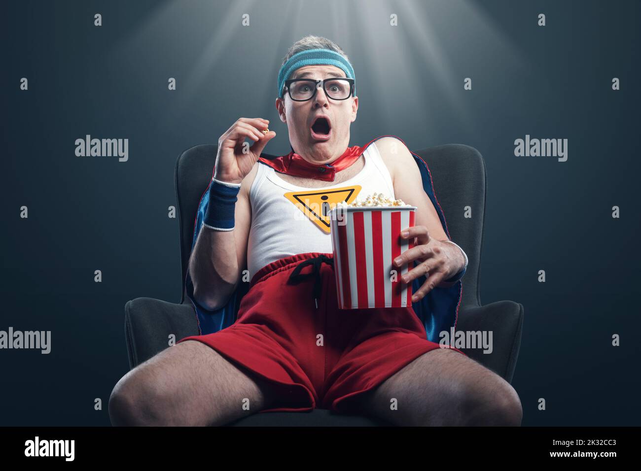 Funny superhero watching horror movies and eating popcorn, he is terrified Stock Photo
