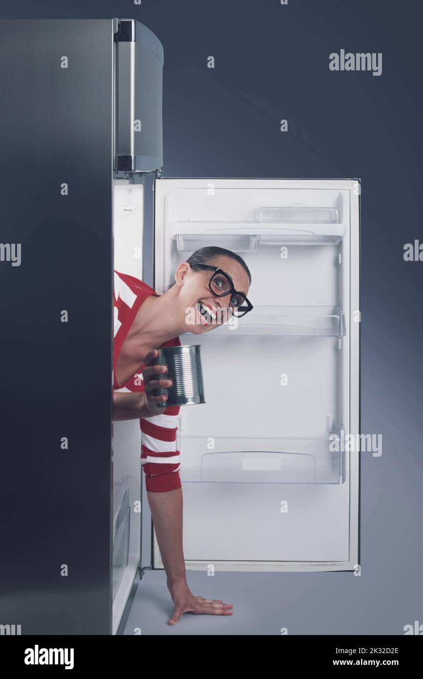 Funny smiling woman inside the fridge, she has found canned food Stock Photo