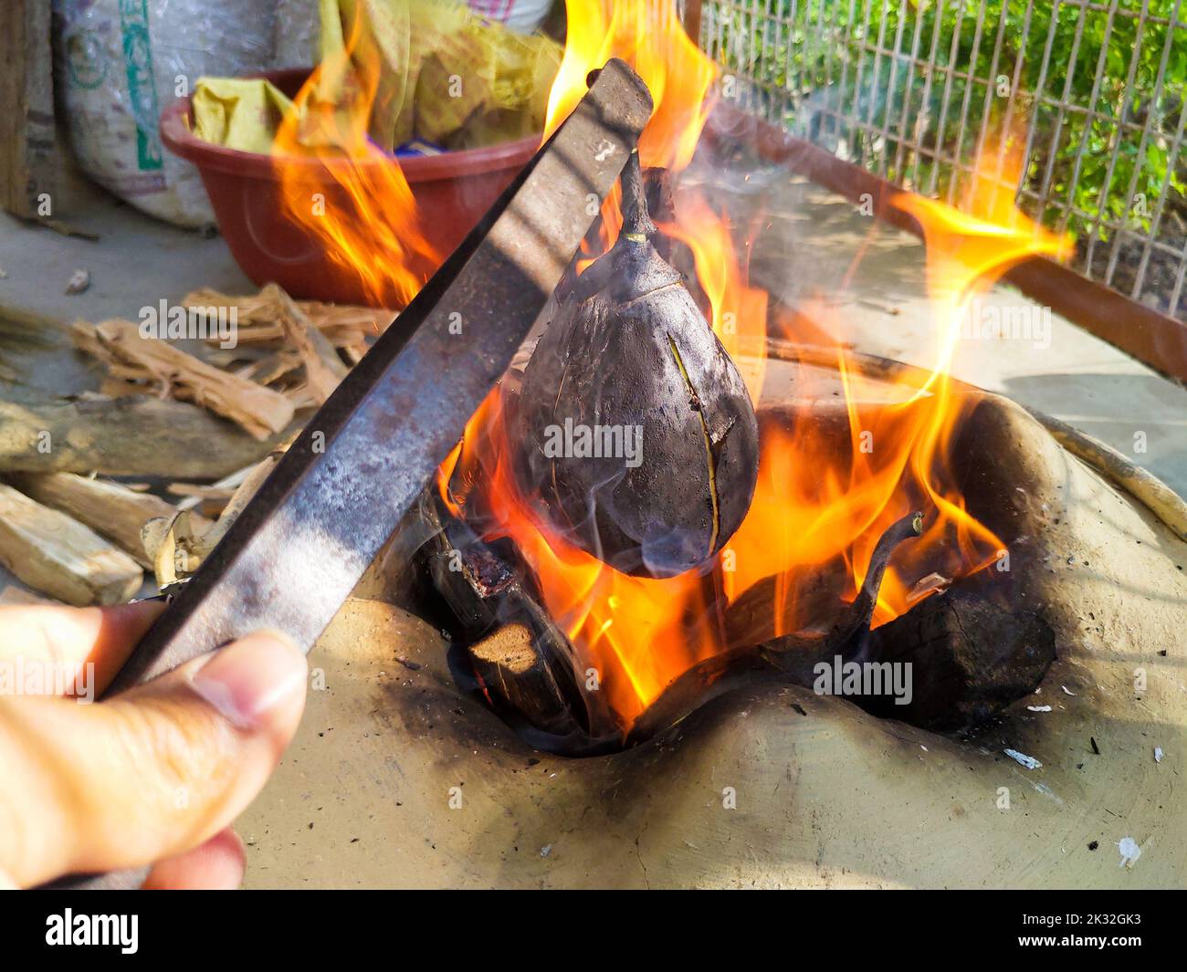 Roasting eggplant using iron tweezers on a traditional firewood stove. Uttarakhand India Stock Photo