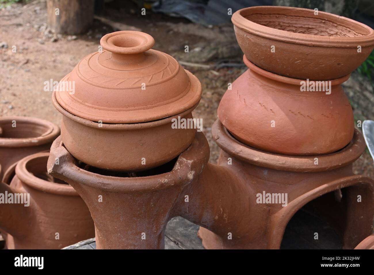A cooking clay pot (pan) with covering lid on top with a another large cooking clay pot on a double clay stove for sell Stock Photo