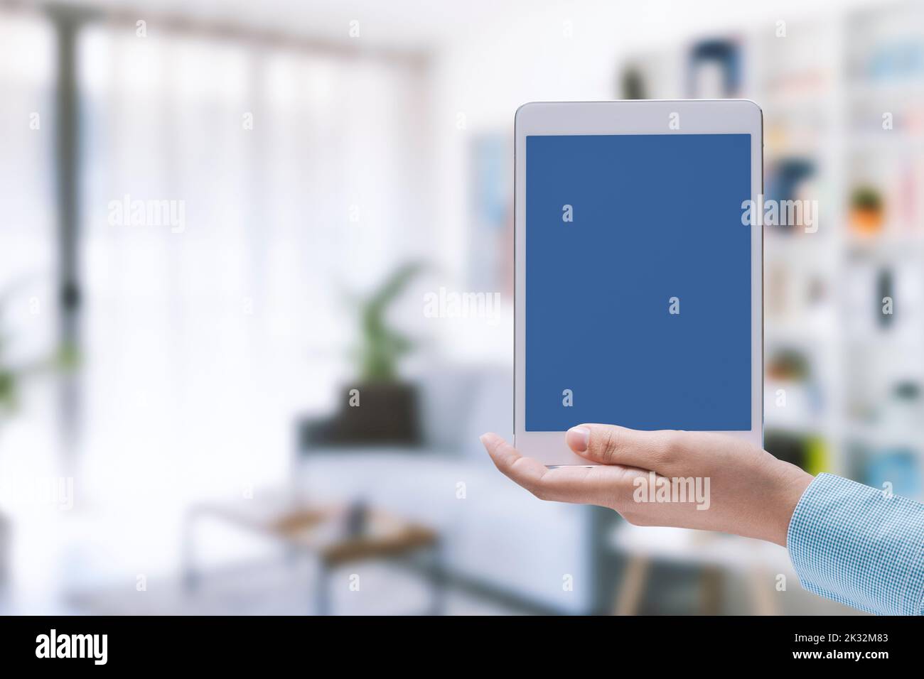Woman holding a tablet with blank screen and house interior, smart home ...