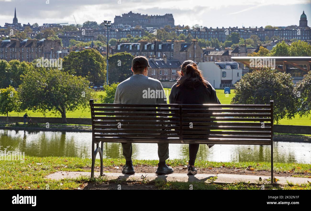Inverleith park, Edinburgh Scotland, UK. 24th September 2022. Morning sunshine after a cloudy start to the day, temperature mid morning around 9 degrees rising to 13 degrees by lunchtime. Pictured this couple relax on a park bench with Inverleith pond and Stockbridge mid ground and the architecture of the city in the background. Credit: Arch White/alamy live news. Stock Photo