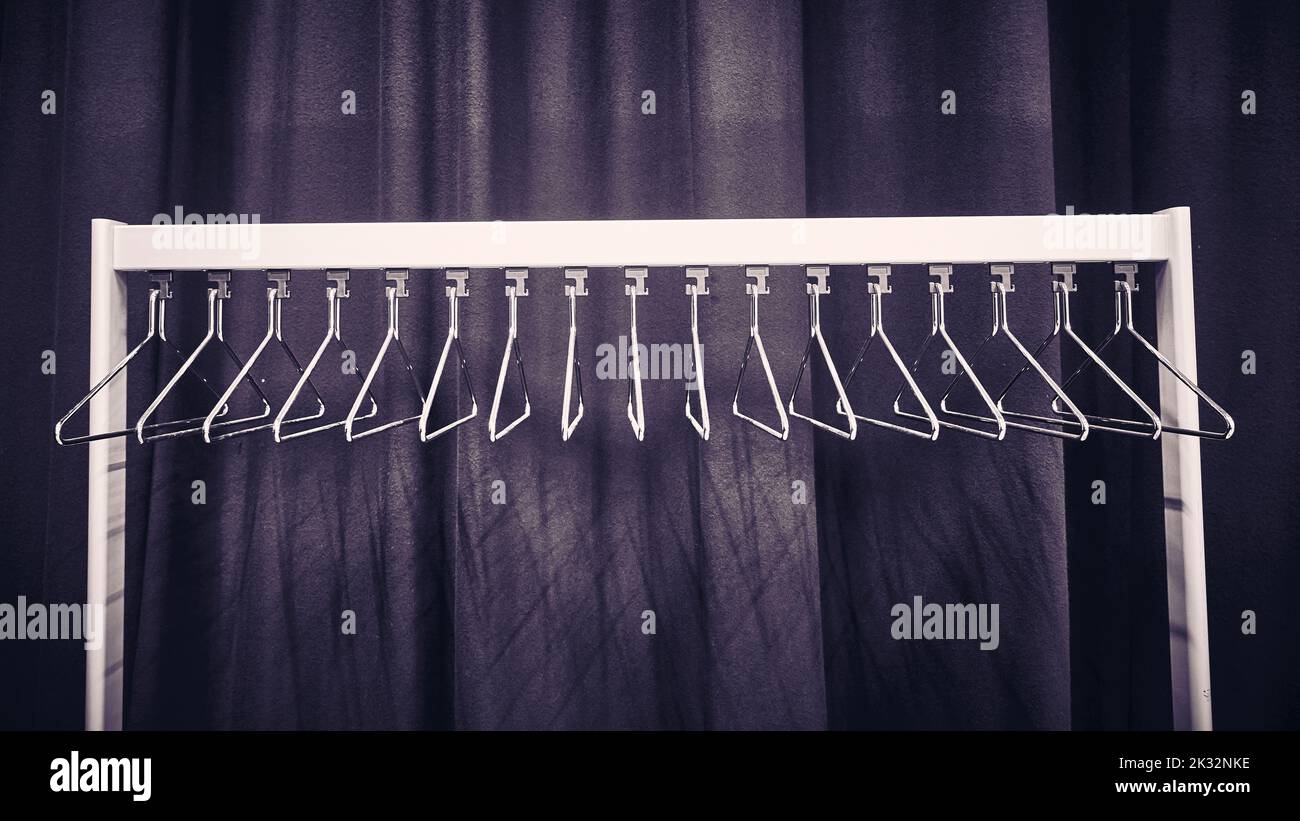 Metal coat hangers on rack in front of dark coloured drapes Stock Photo